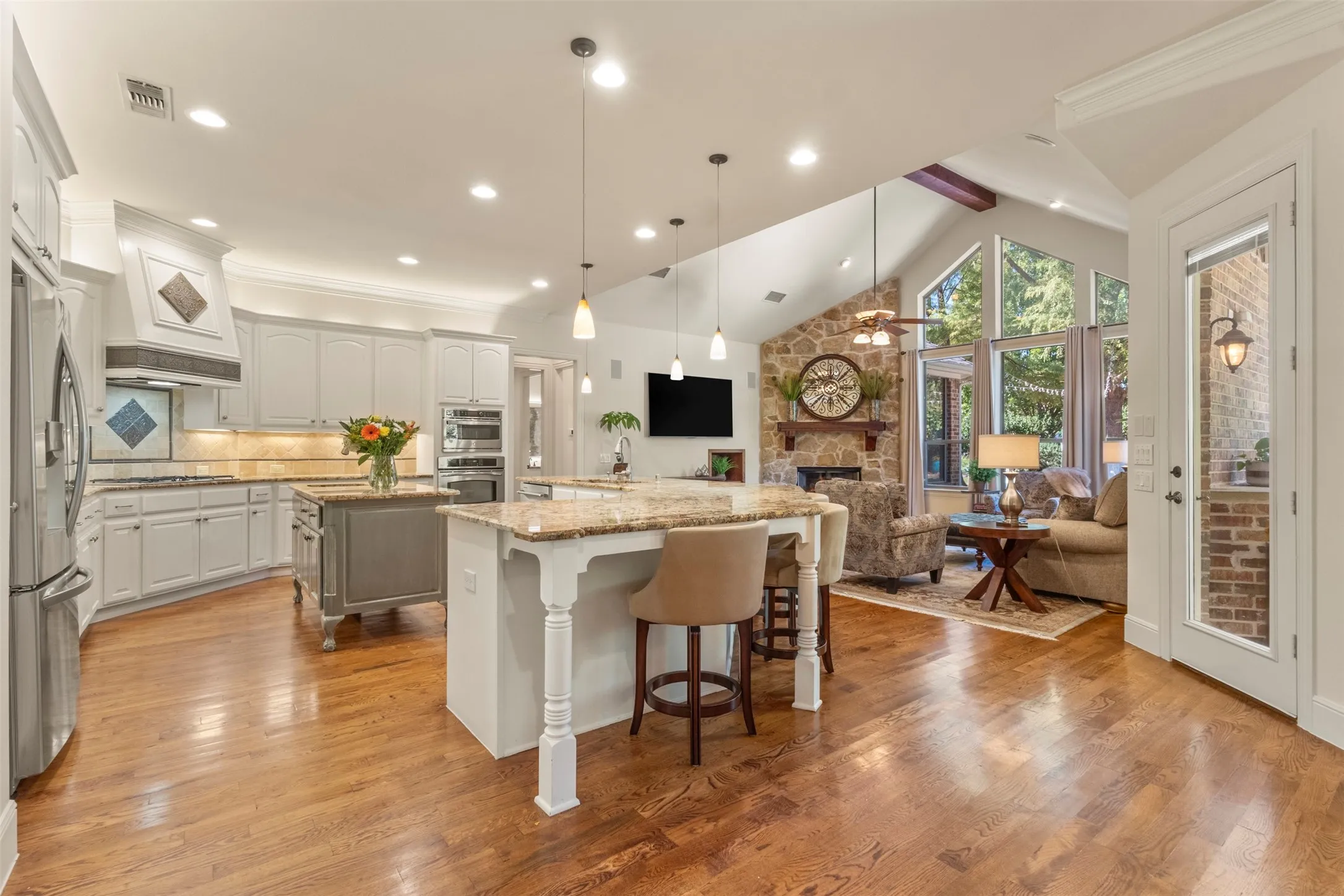 Hardwood flooring with a vaulted ceiling, stone-faced fireplace, and built-in double ovens
