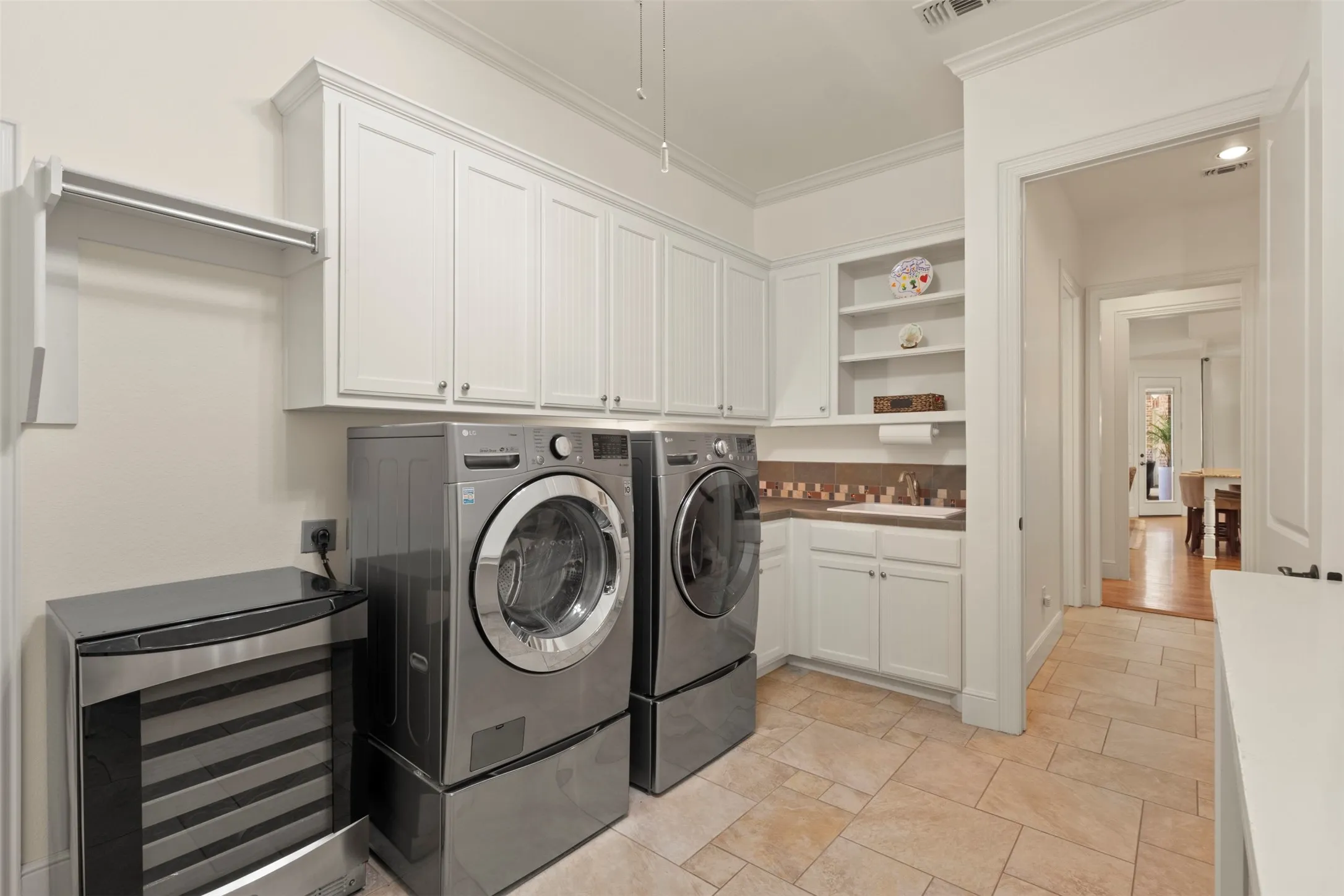 Laundry room featuring tile flooring, white cabinetry, a built-in folding rack, and a utility sink with a tiled backsplash