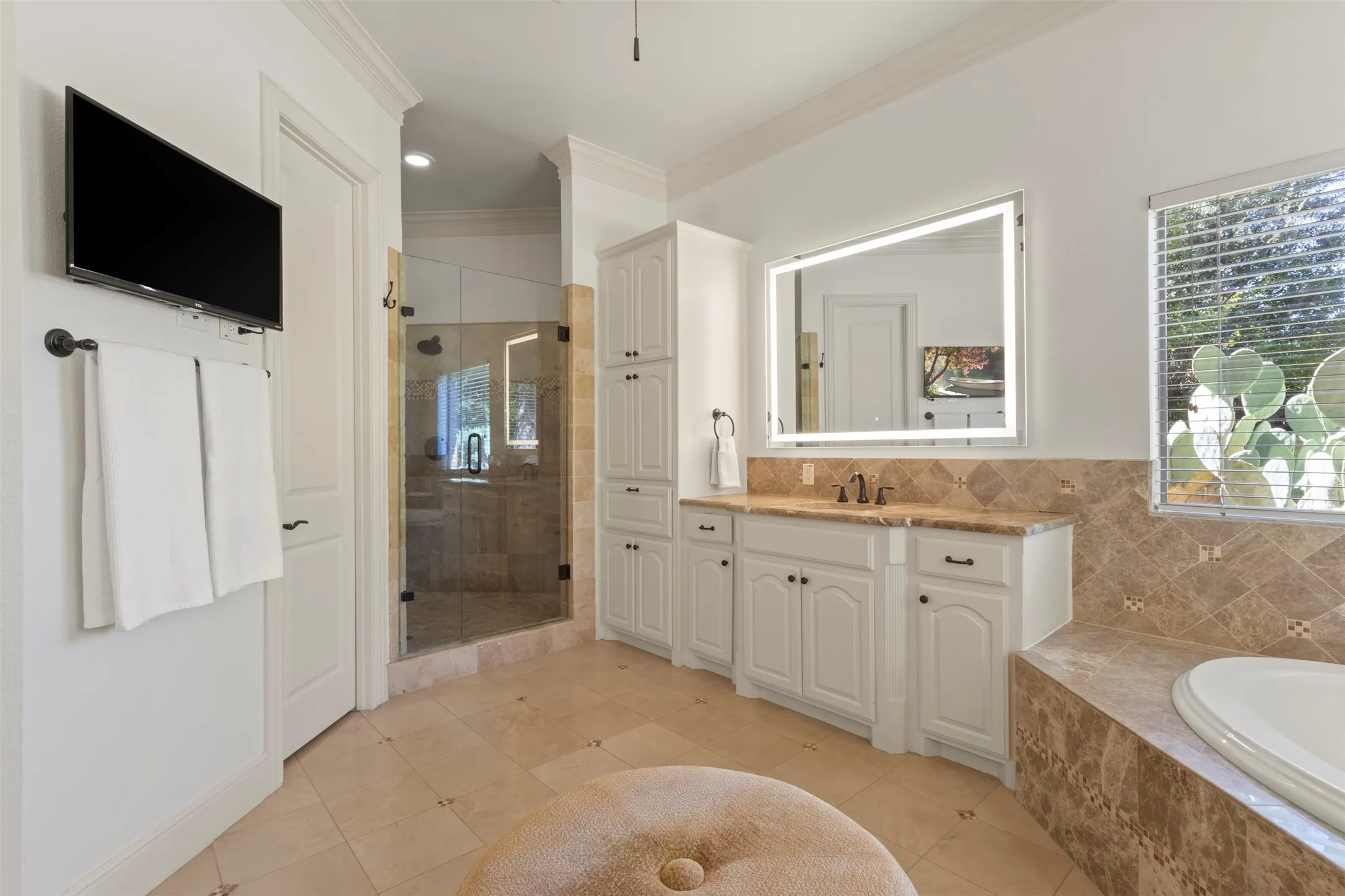 Tile flooring, white vanity with integrated sink, freestanding soaking tub, glass-enclosed shower, and built-in storage cabinetry