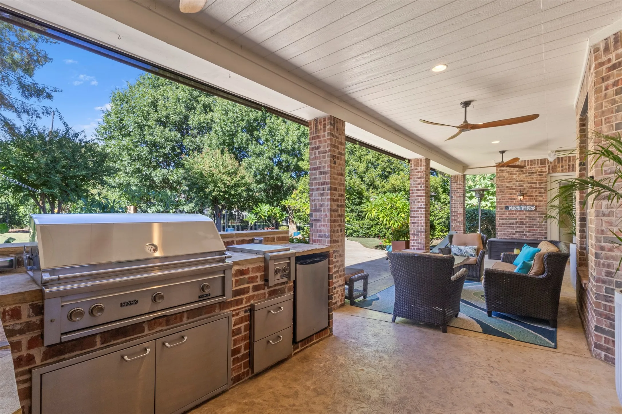 Covered outdoor patio featuring brick pillars, wood-paneled ceiling, and two ceiling fans