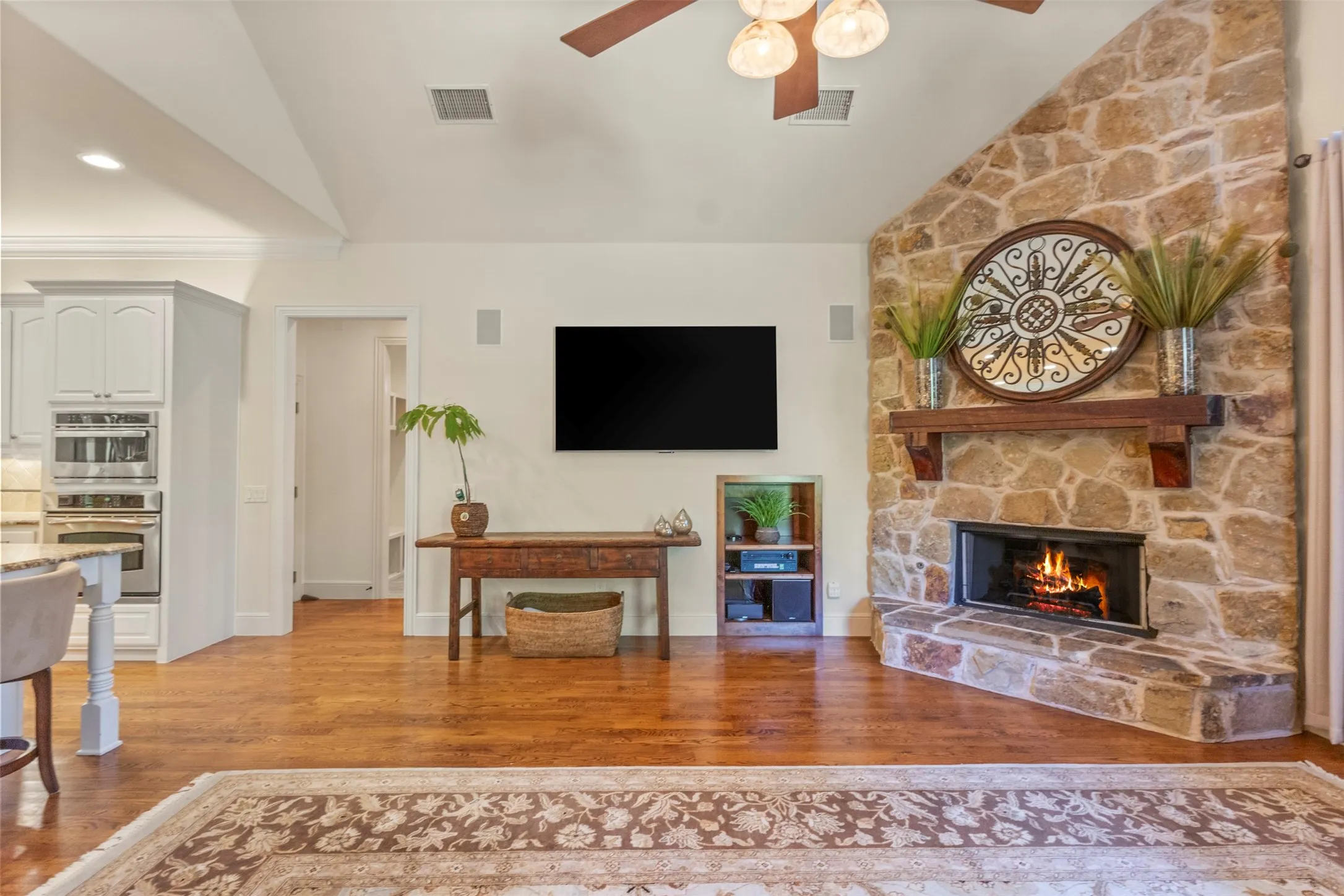 Warm wood-finish flooring, a stone-clad fireplace with a wood mantel, and vaulted ceilings