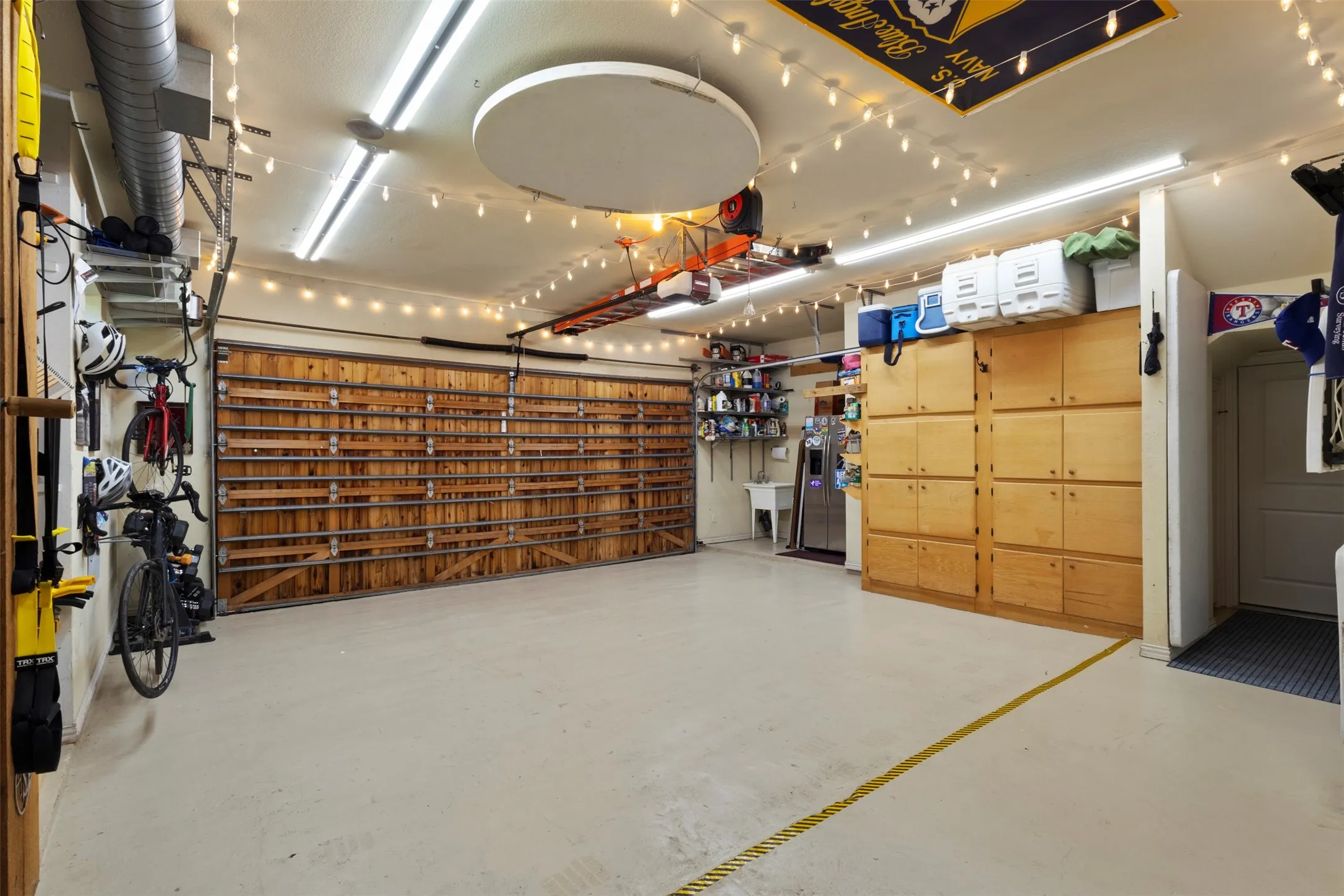 Spacious garage with light-toned flooring, extensive built-in cabinetry, and a utility sink