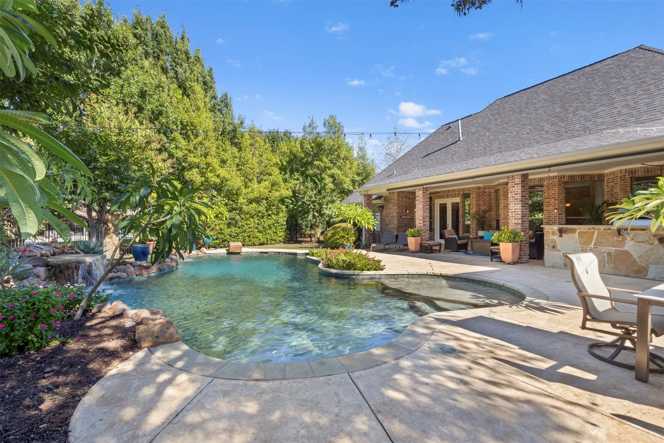 Expansive backyard featuring a custom pool with a rock waterfall, a built-in spa, a large concrete patio, and a covered porch with brick columns