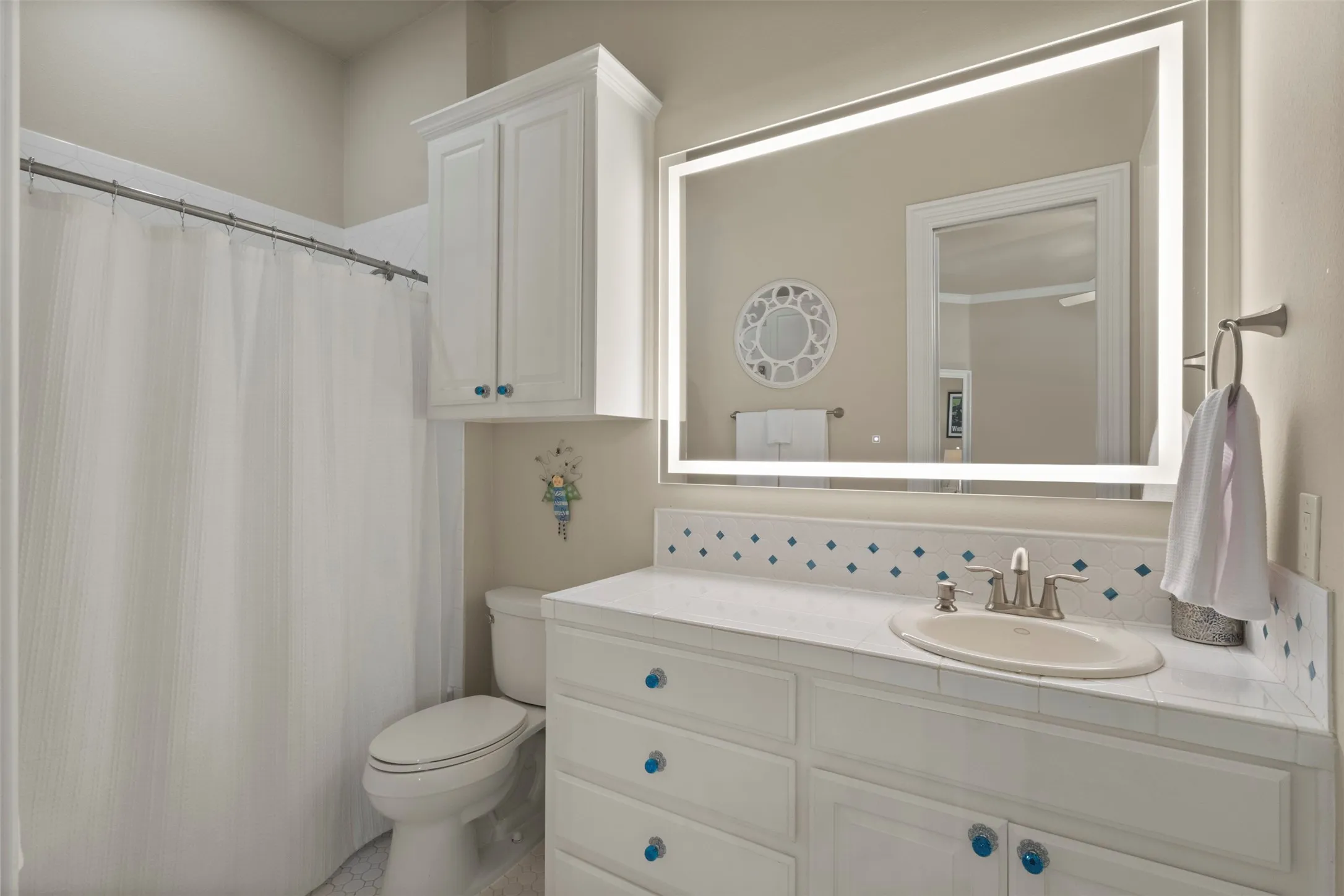 Vanity with an integrated sink, illuminated mirror, and white cabinetry