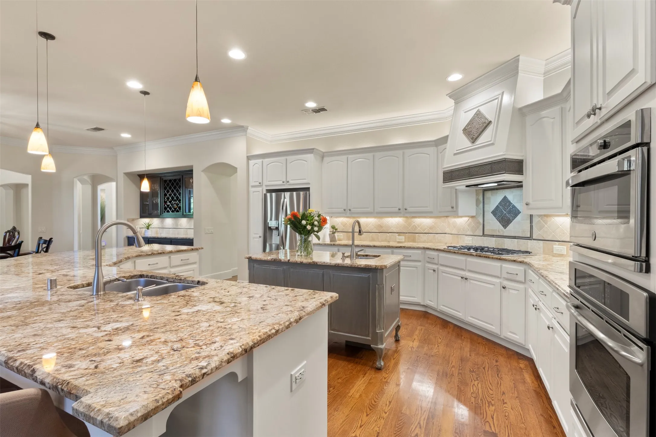 Kitchen with light-toned cabinetry, a spacious island with a double basin sink, and wood-finish flooring