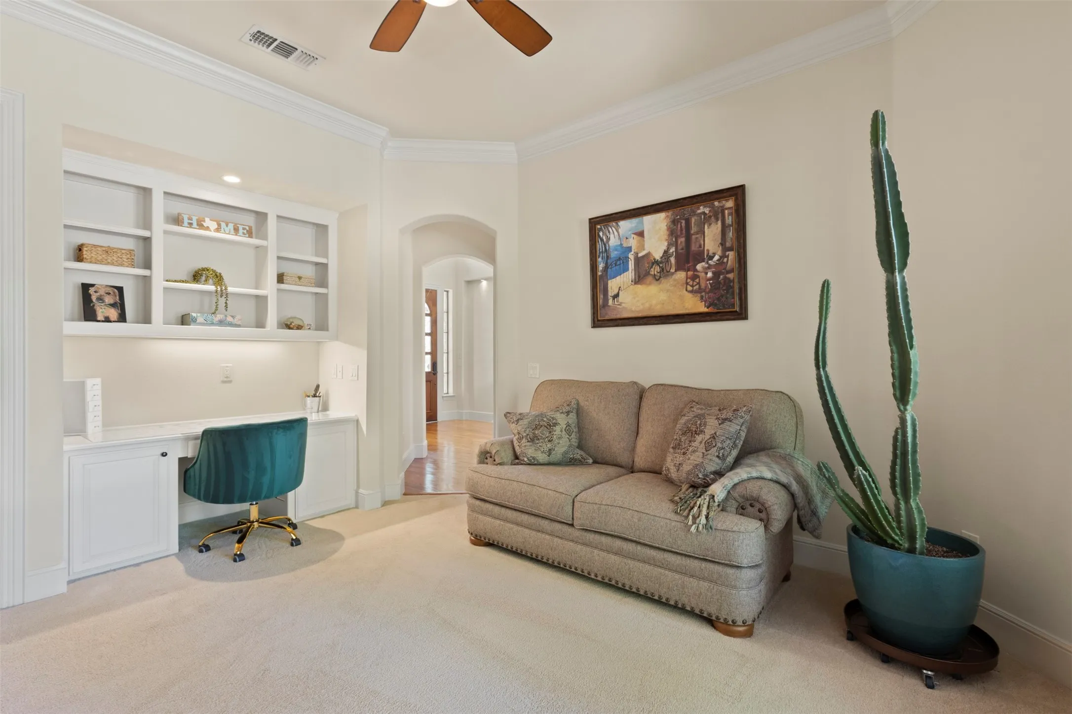 Built-in desk with integrated shelving and task lighting, arched doorway, crown molding, and ceiling fan