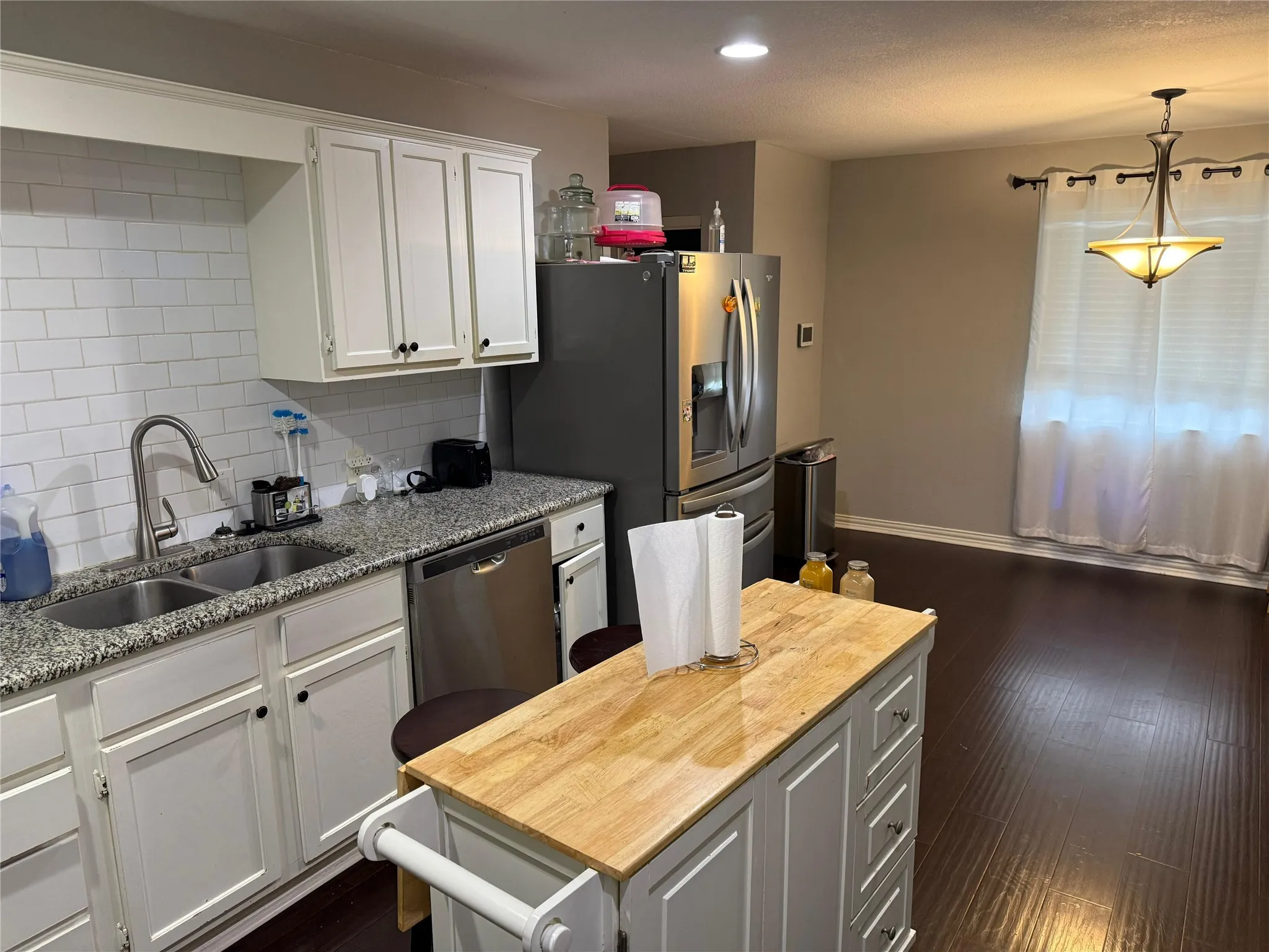 White shaker-style cabinetry with black hardware, granite countertops, stainless steel appliances, and a subway tile backsplash