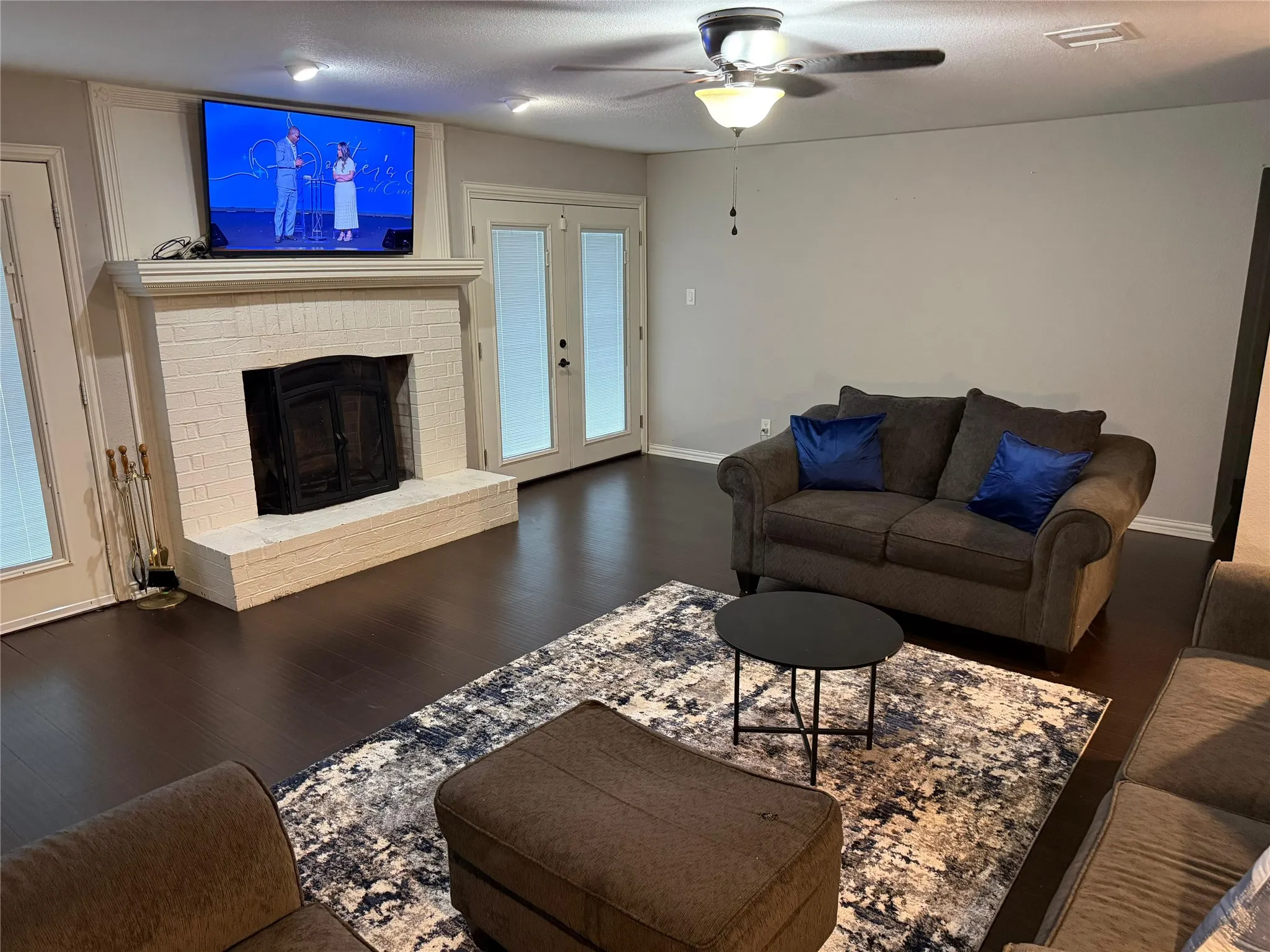 Living area featuring wood-finish flooring, a white brick fireplace, and dual French doors