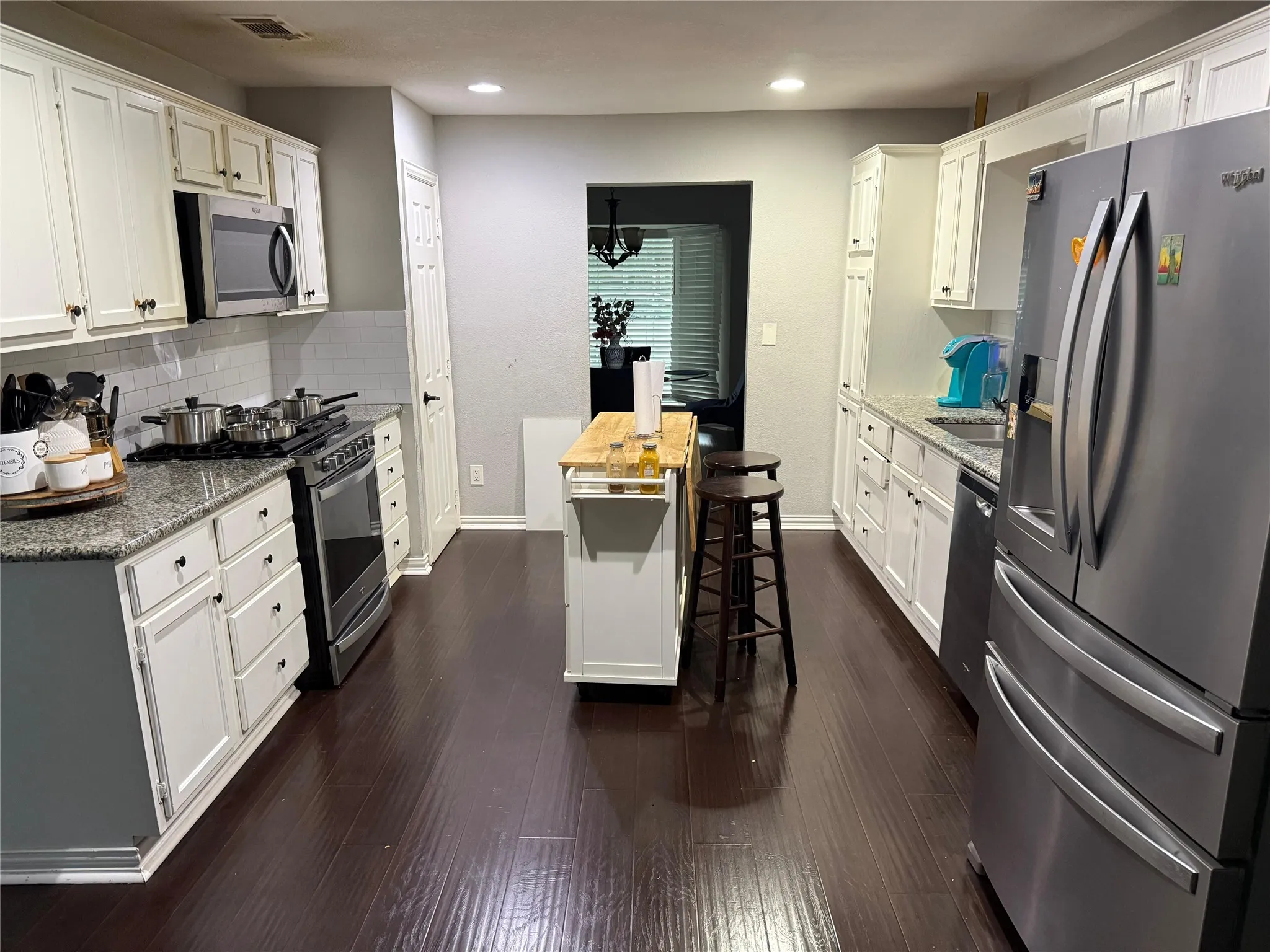 Kitchen with wood-finish flooring, white cabinetry, granite countertops, and stainless steel appliances