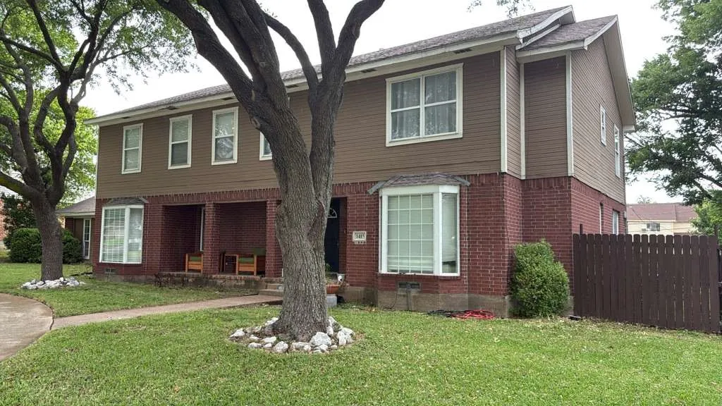 Two-story exterior with brick and siding facade, mature trees, a bay window, and a fenced perimeter