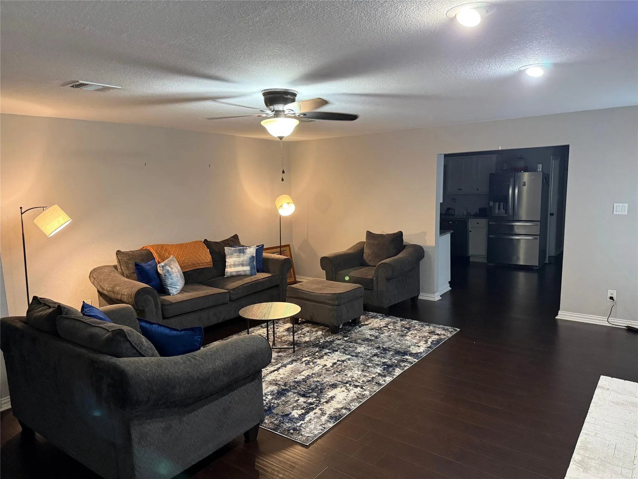 Spacious living area featuring dark wood-finish flooring, ceiling fan with integrated lighting, and recessed ceiling lights