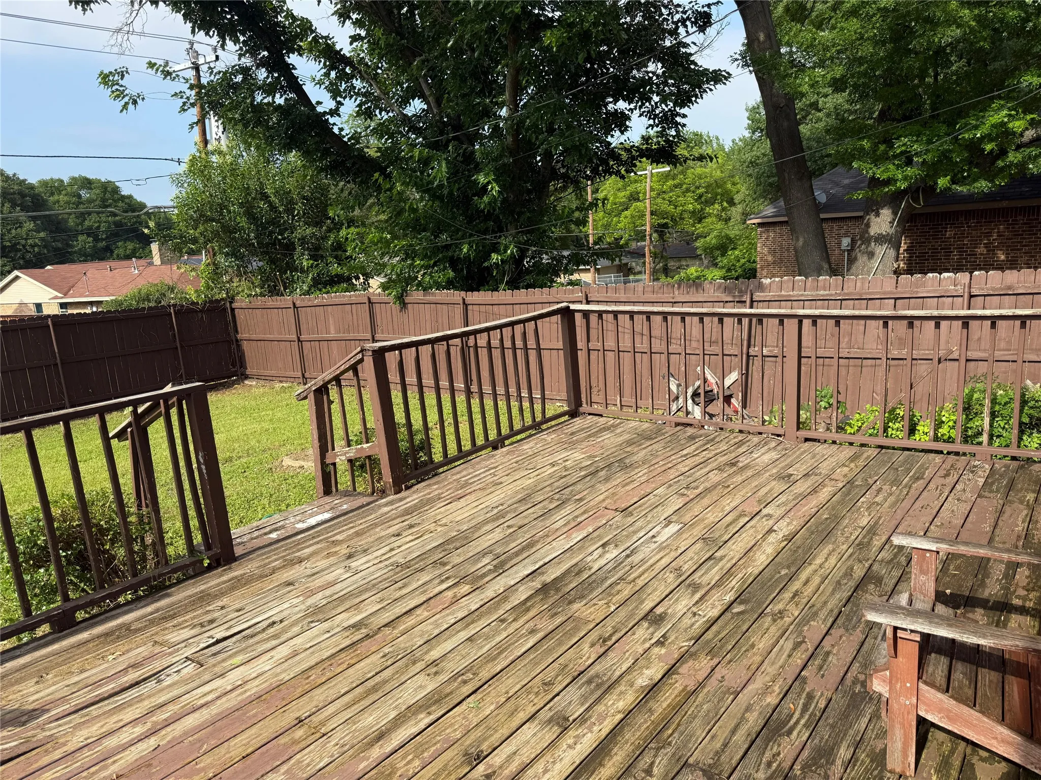Expansive wooden deck with railings, fenced yard, and mature trees