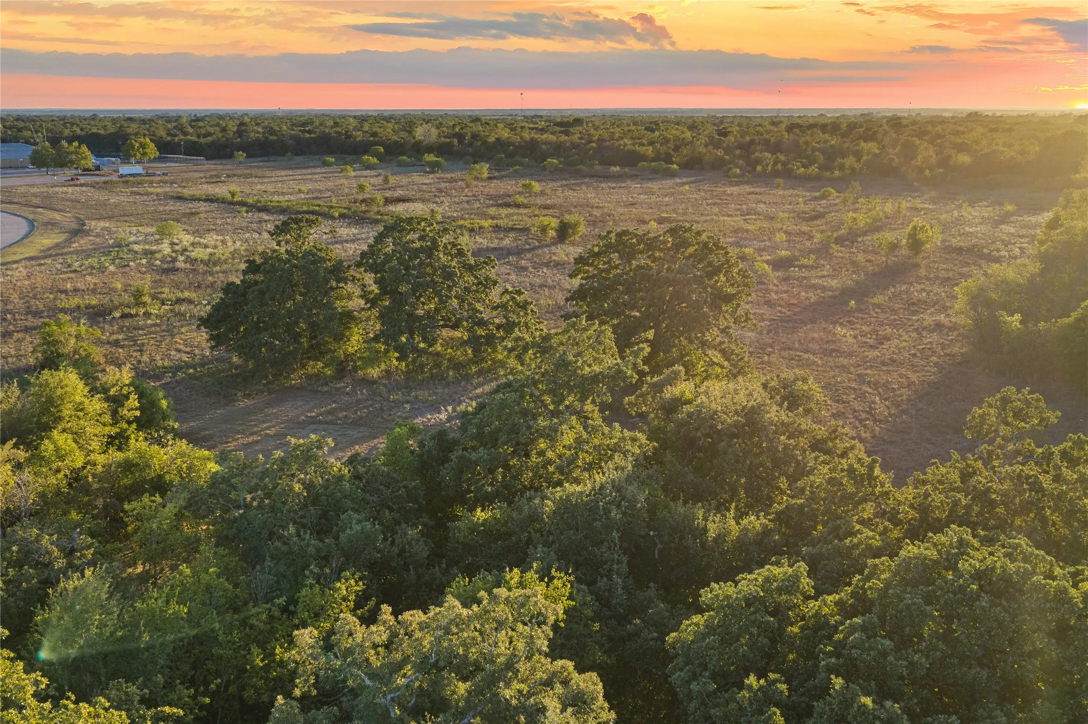 Expansive acreage featuring mature trees and open fields under a vibrant sky