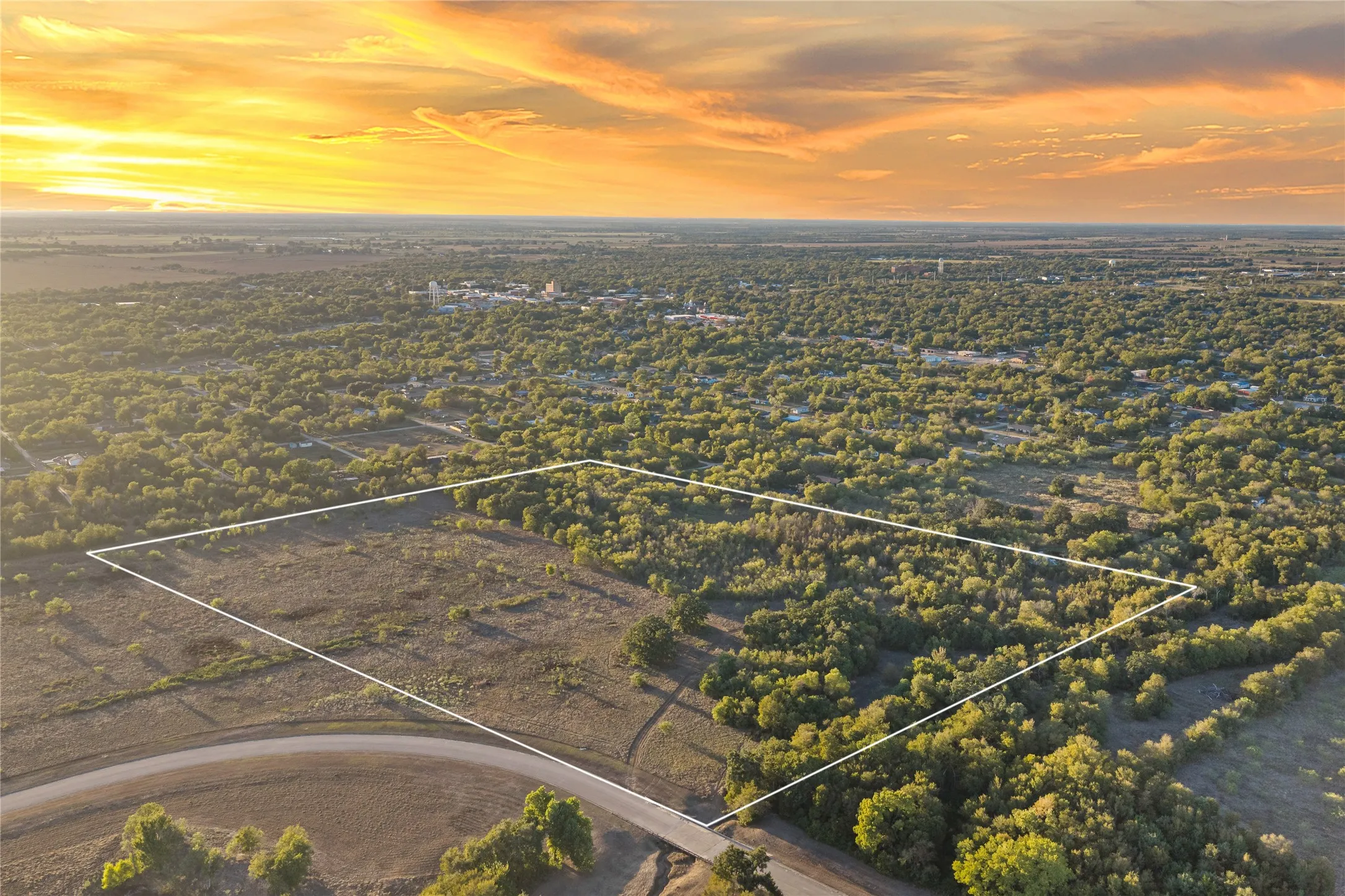 Expansive undeveloped land featuring a mix of open areas and mature trees, bordered by a paved road