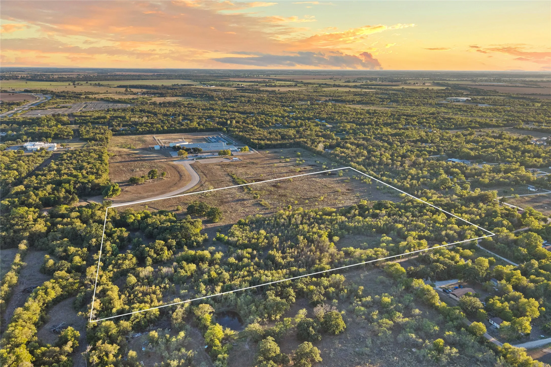 Expansive undeveloped land with diverse tree coverage and partially cleared areas, featuring a small pond