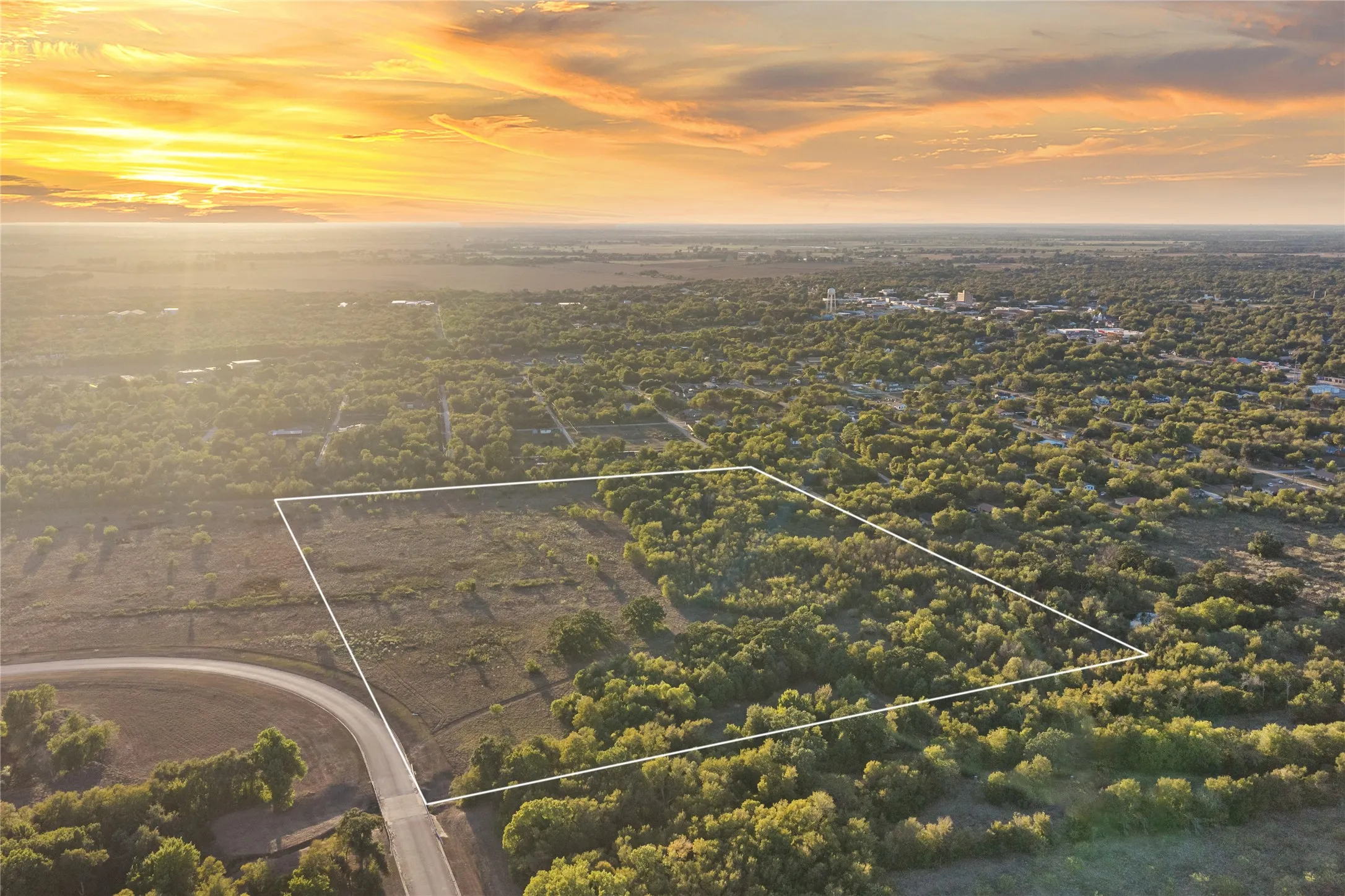 Expansive undeveloped land featuring a mix of open areas and mature trees, bordered by a paved road