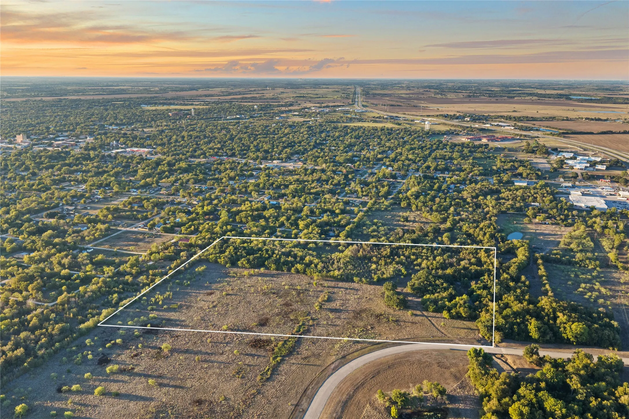 Expansive land parcel featuring a mix of open areas and mature trees, bordered by established residential and commercial infrastructure
