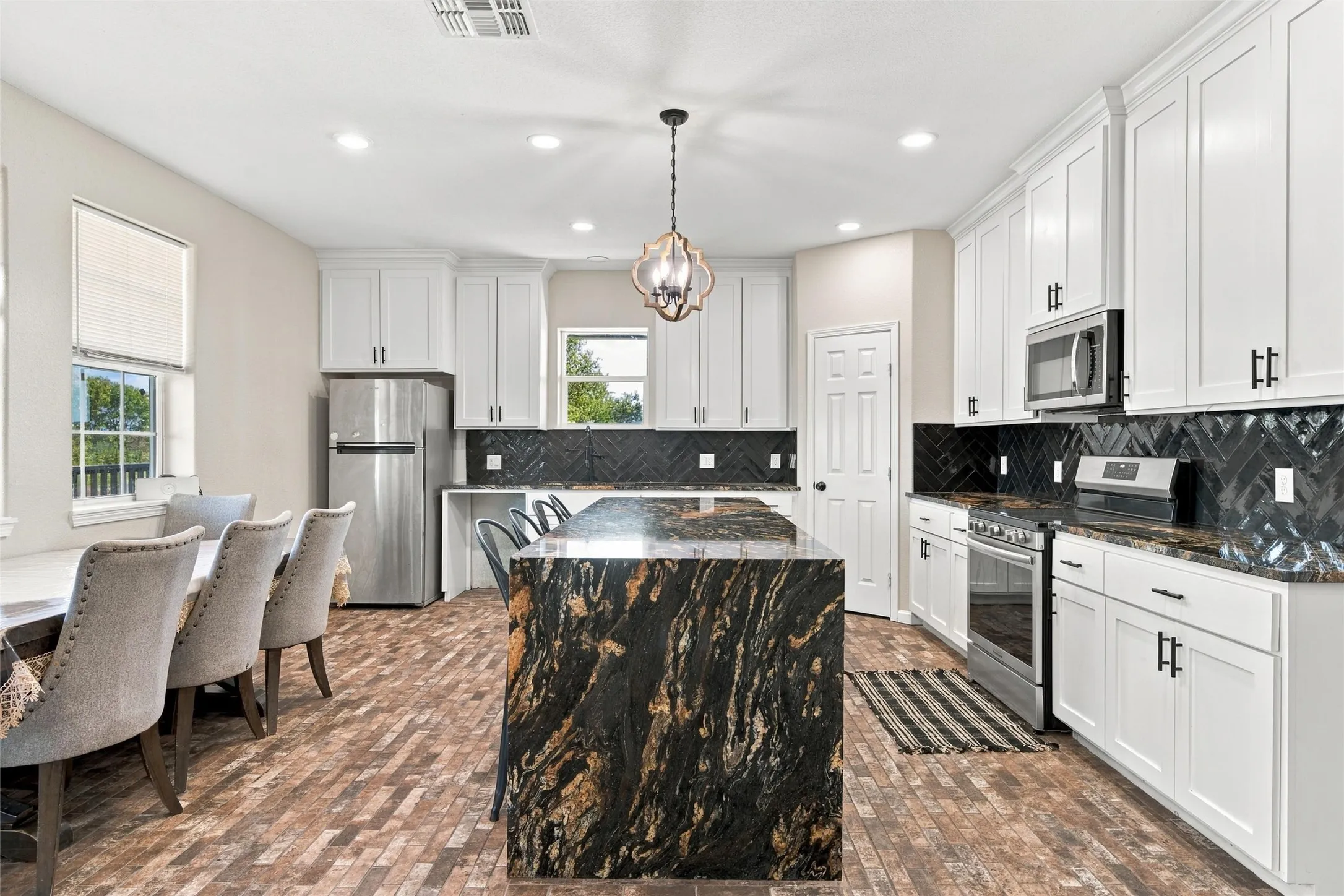 Kitchen featuring white cabinetry, dark stone countertops, stainless steel appliances, a dark herringbone tile backsplash, and a substantial island with stone surfacing
