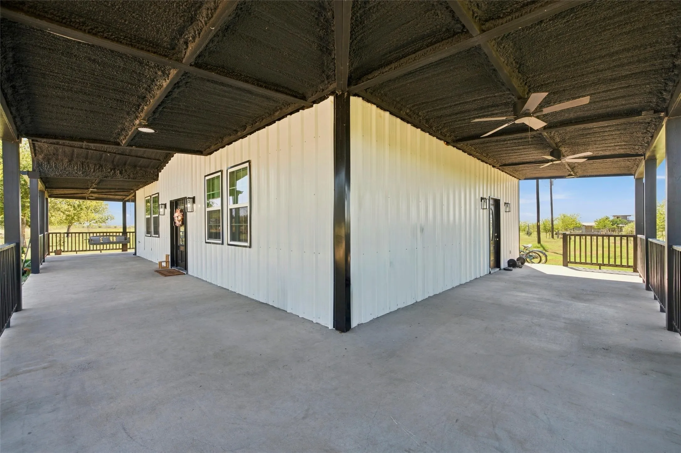 Expansive covered concrete patio with ceiling fans, black metal railings, and dual exterior entry doors