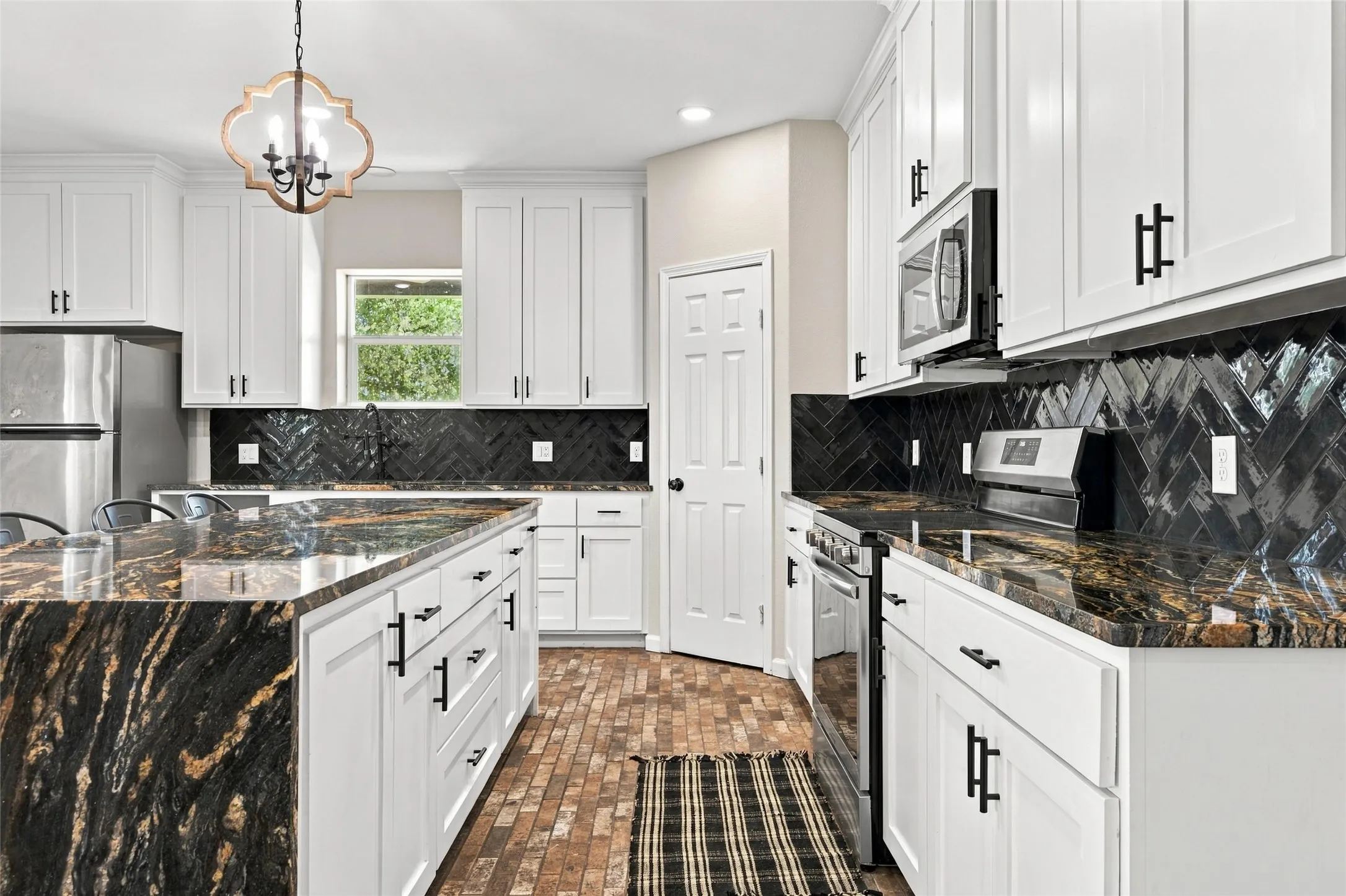 White cabinetry with black hardware, black herringbone tile backsplash, stainless steel appliances, and a large central island with a waterfall edge and stone countertop