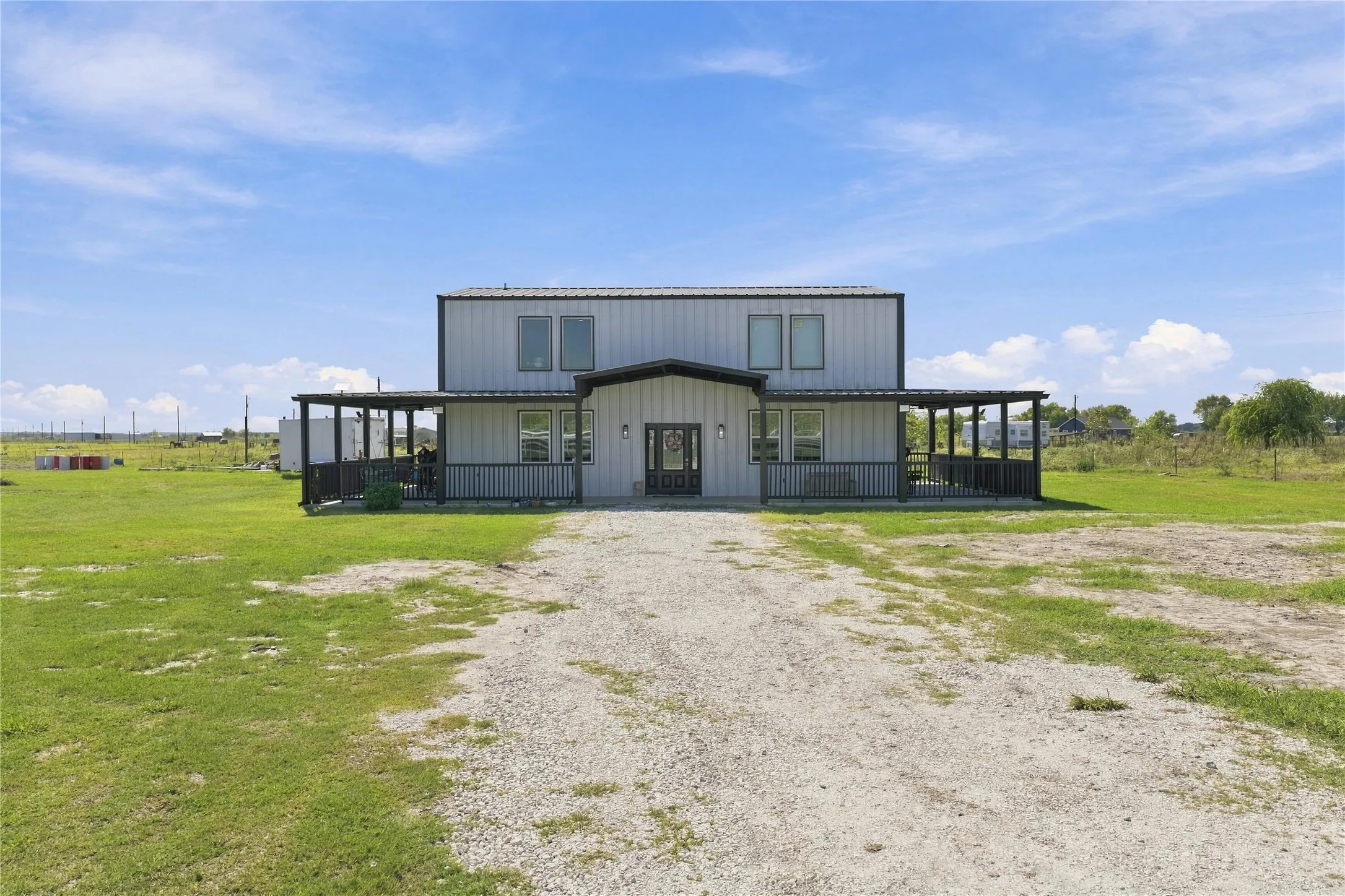 Metal siding exterior with a dark trim wrap-around porch and a gravel driveway