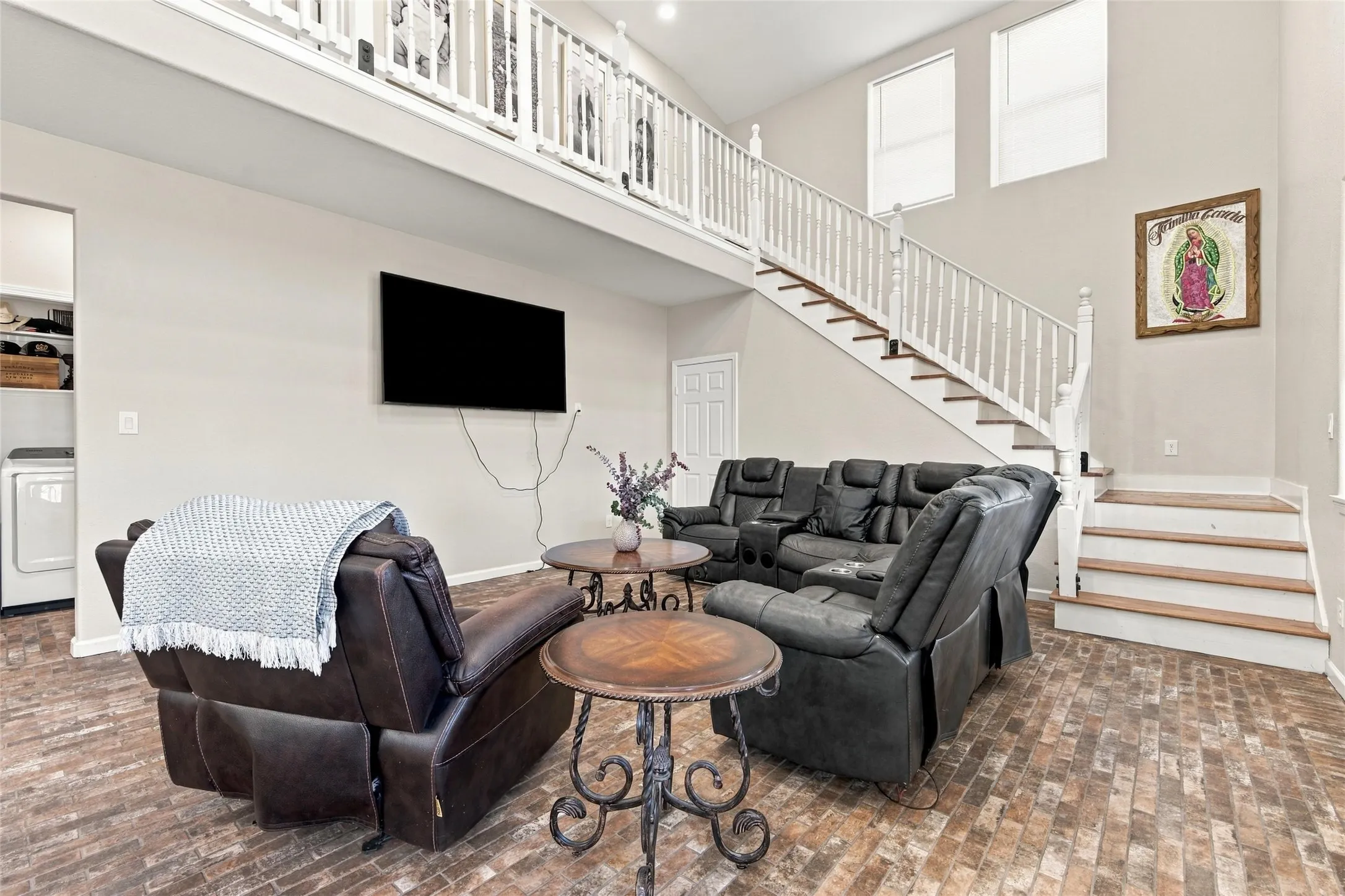 Open-concept living area featuring a two-story ceiling, a staircase with white railings, and high-set windows