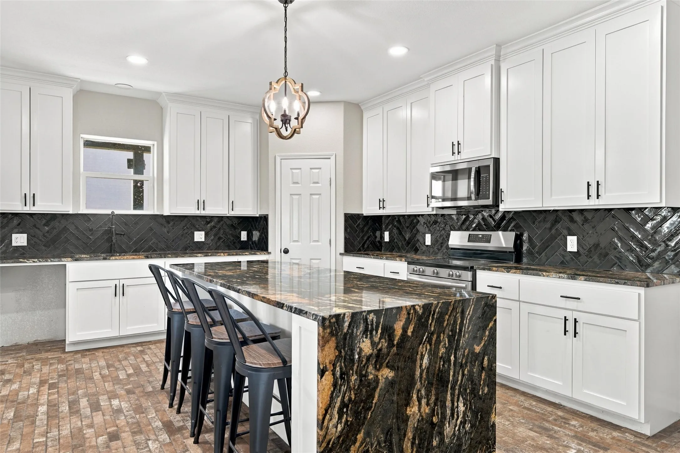 Kitchen featuring white cabinetry, dark herringbone tile backsplash, and a multi-toned stone island with an integrated breakfast bar