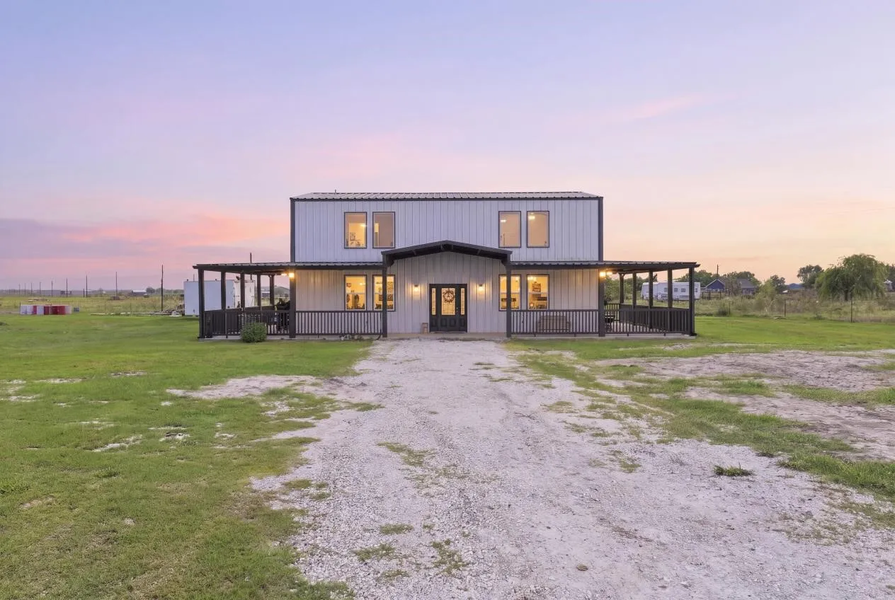 Modern farmhouse-style exterior with a covered front porch, dark railings, and a gravel driveway