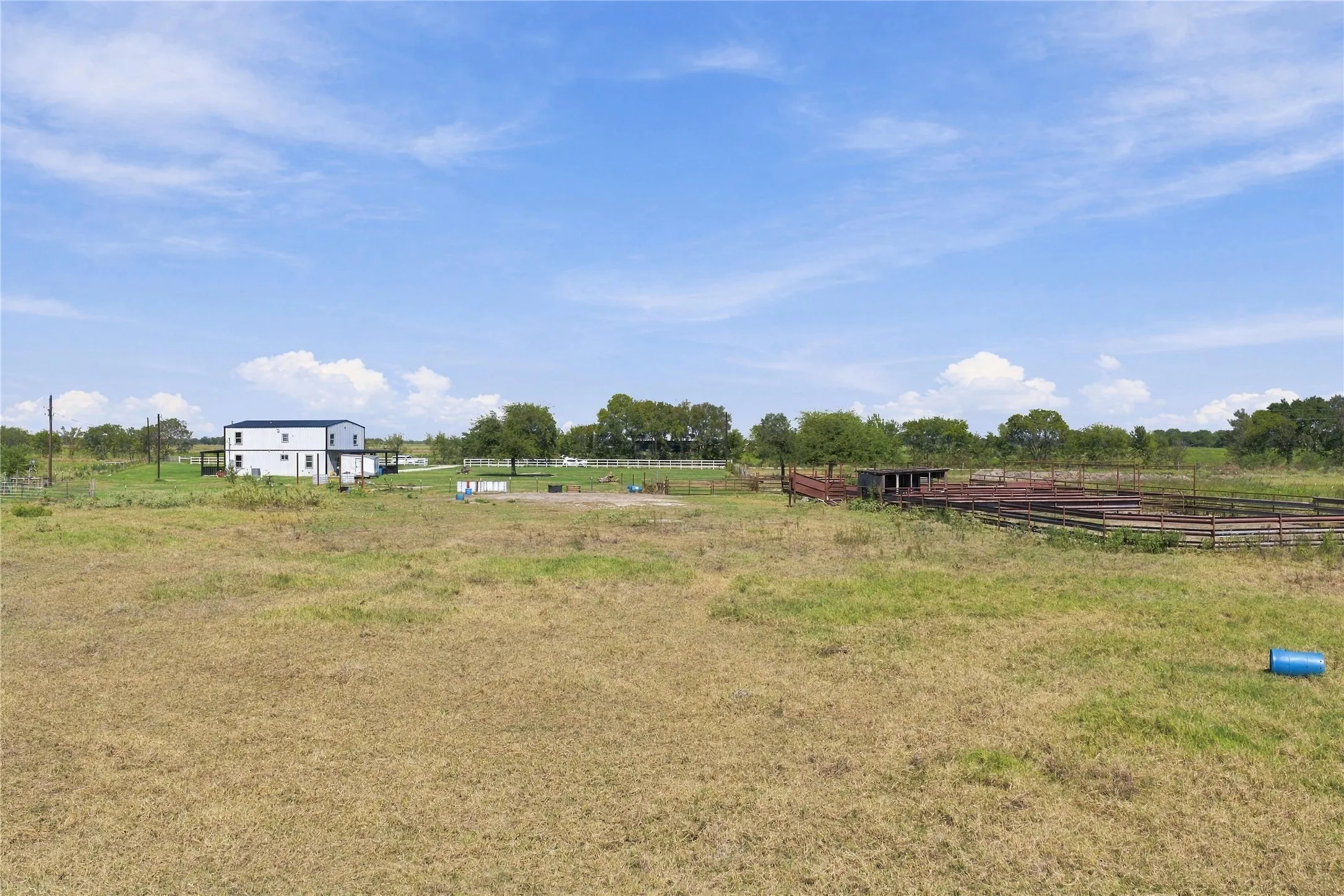 Two-story residence with a dark roof and light siding, surrounded by expansive grassland