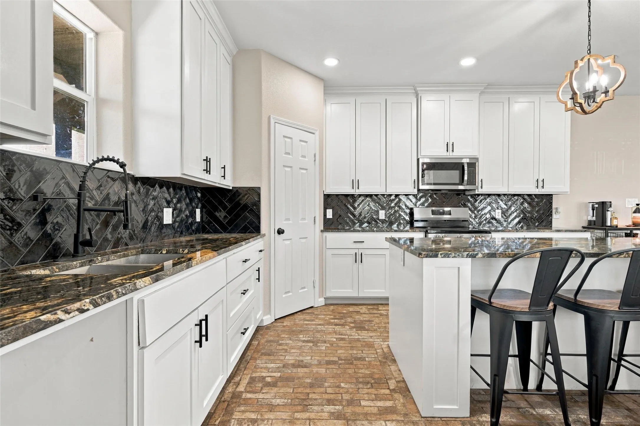 Kitchen featuring white shaker-style cabinetry, black chevron tile backsplash, dark multi-tone stone countertops, and a central island with counter seating