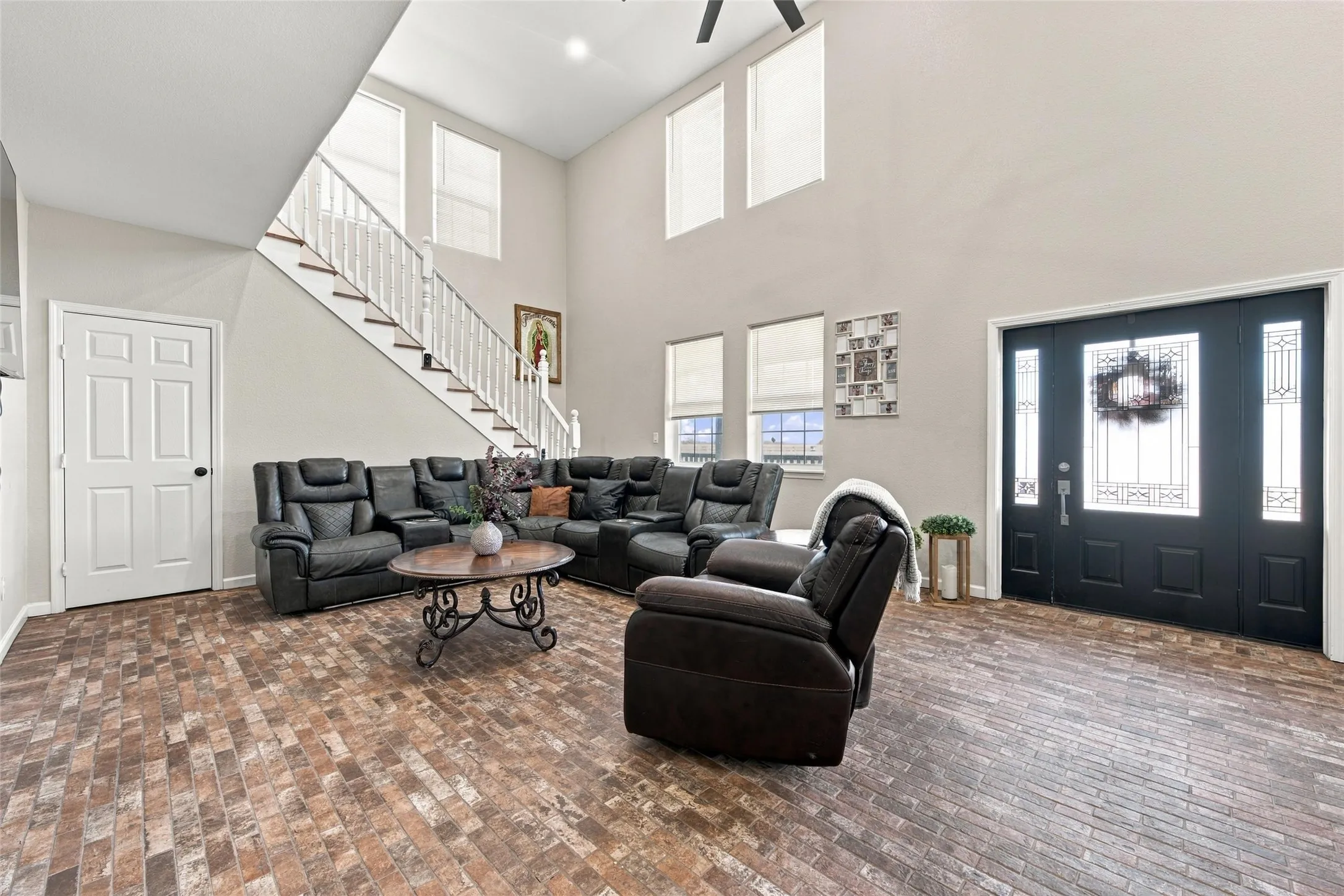 Vaulted ceilings, brick-style flooring, white staircase with wood treads, multi-paneled front entry door with sidelights, and multiple windows