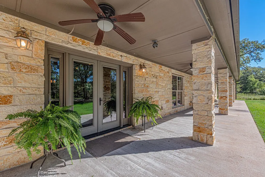 Expansive property featuring a single-story residence with a covered porch, a separate outbuilding, a concrete driveway, and a large grassy area surrounded by abundant mature trees