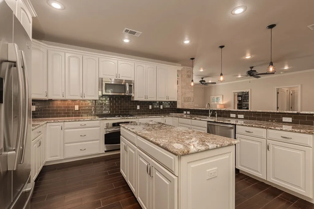Modern kitchen featuring white cabinetry, stainless steel appliances, granite countertops, and wood-finish flooring