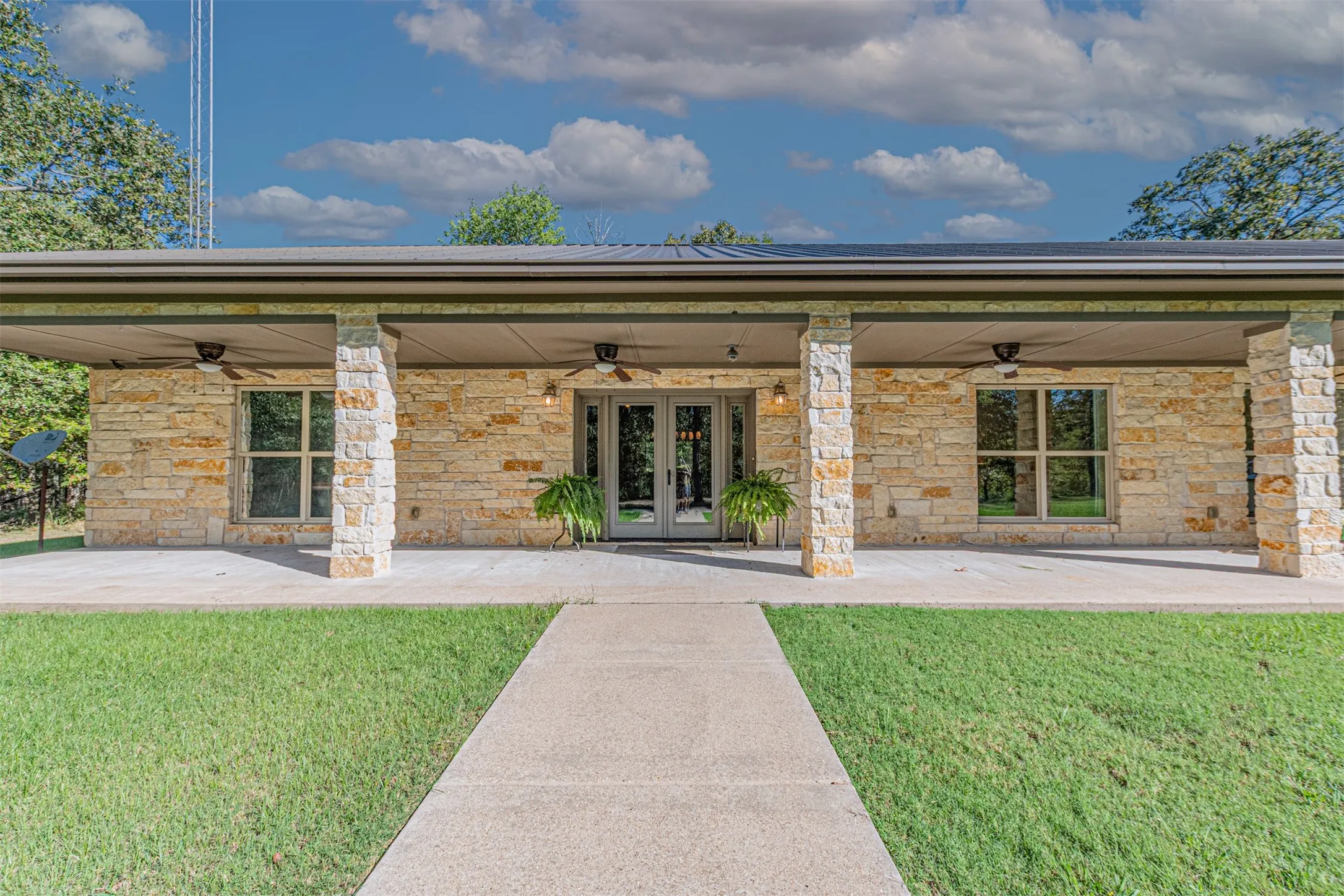 Stone facade with a covered patio, multiple ceiling fans, and concrete walkway