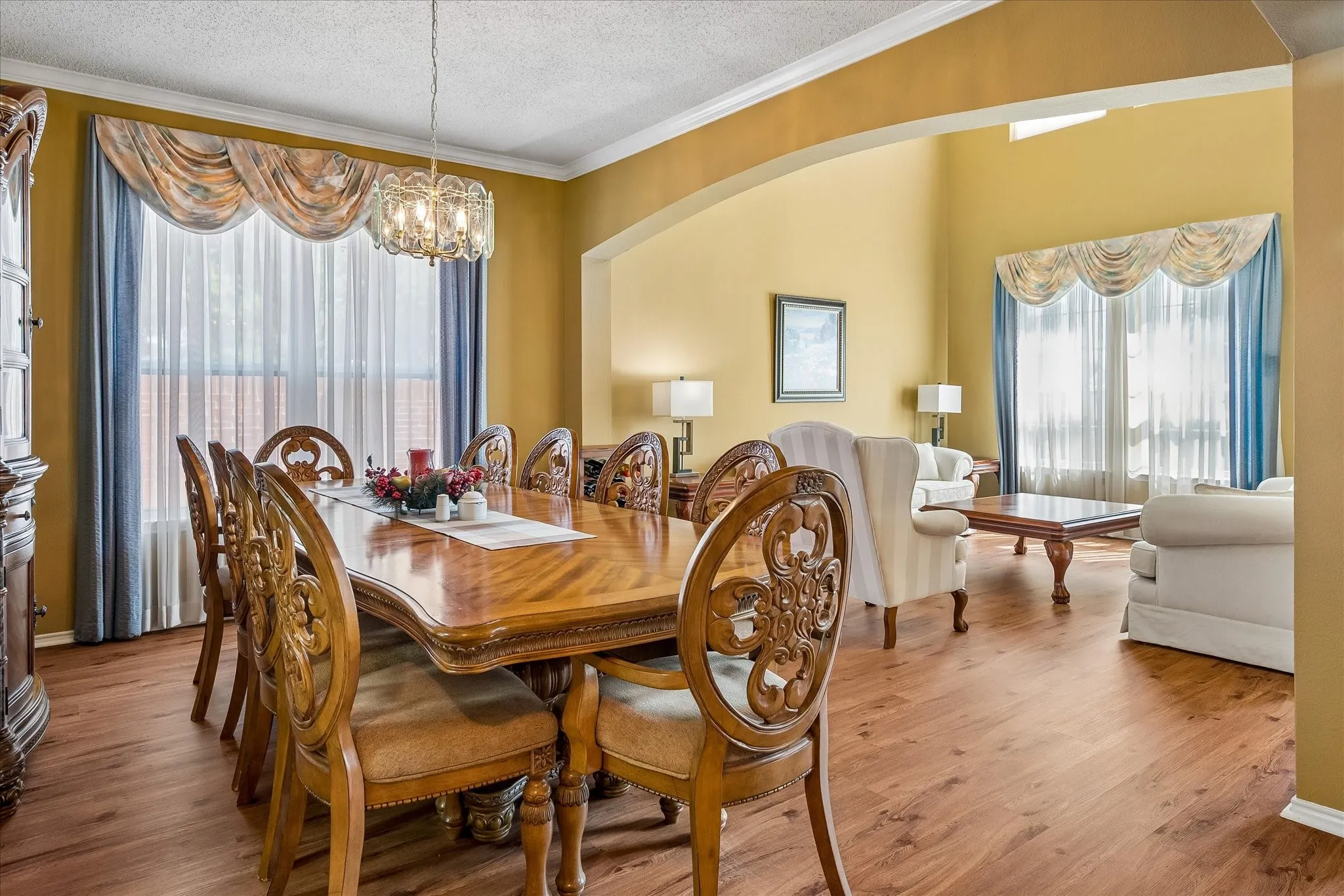 Wood-finish flooring throughout, with a crystal chandelier, arched doorway, and crown molding