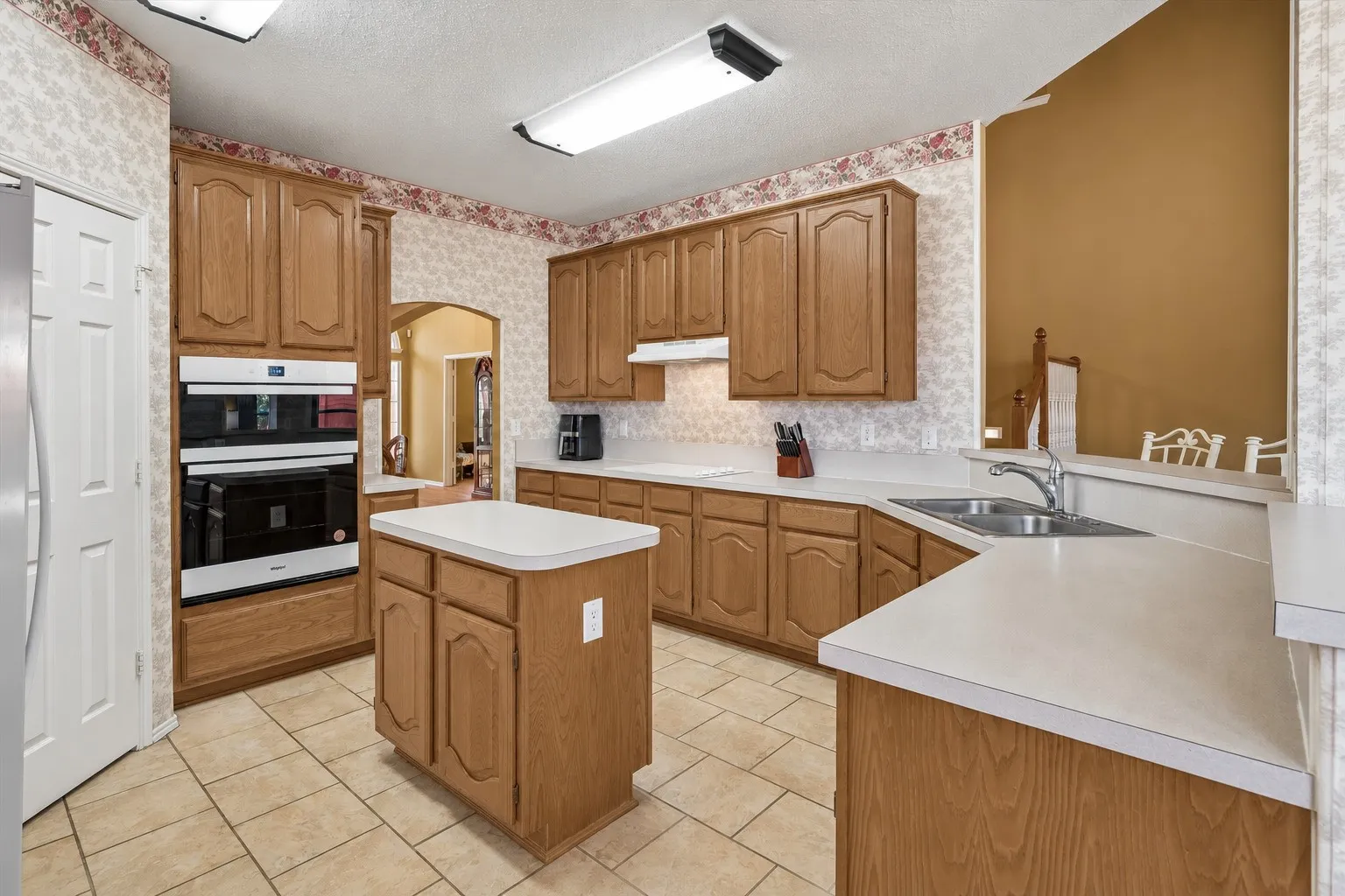 Kitchen featuring wood cabinetry, light countertops, a double wall oven, a central island, and tile flooring