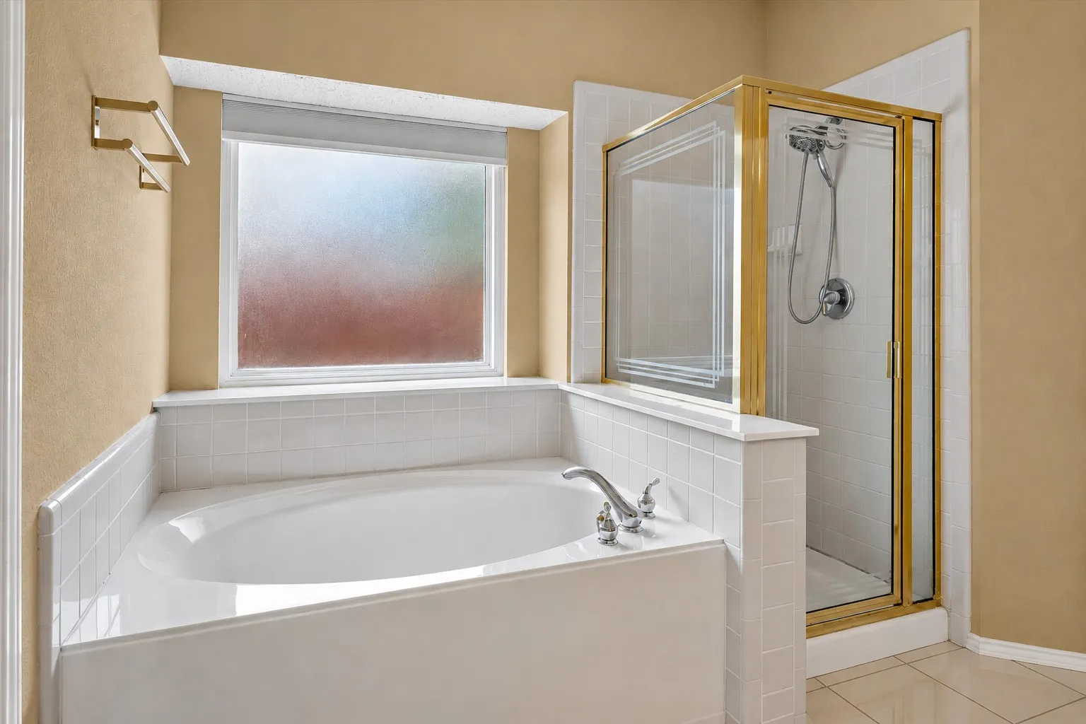 Soaking tub with tile surround, separate shower with framed glass enclosure, and frosted window
