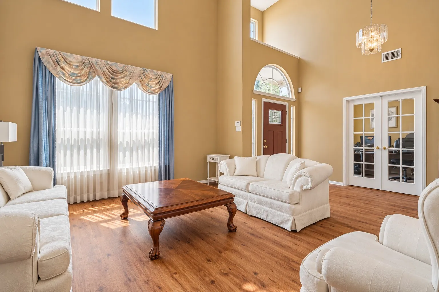 Vaulted ceilings with upper windows, wood-finish flooring, French doors with transom, and a paneled entry door with an arched transom