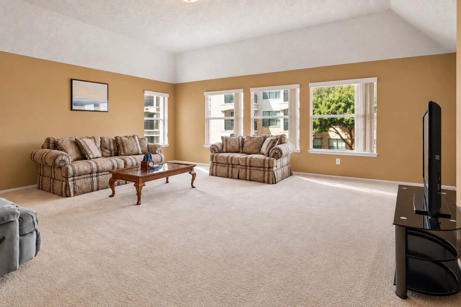 Vaulted ceiling, multiple windows, beige wall color, and light-toned carpeting