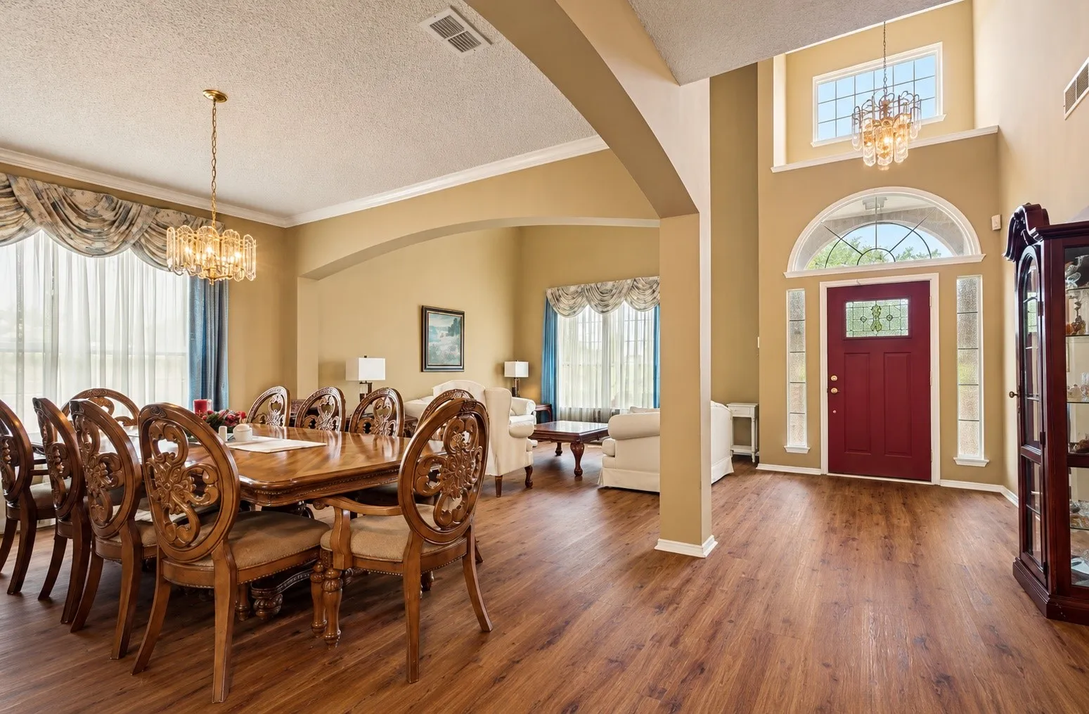 Two-story foyer with transom window and sidelights, wood-finish flooring, arched entryway, and a formal dining area with a crystal chandelier