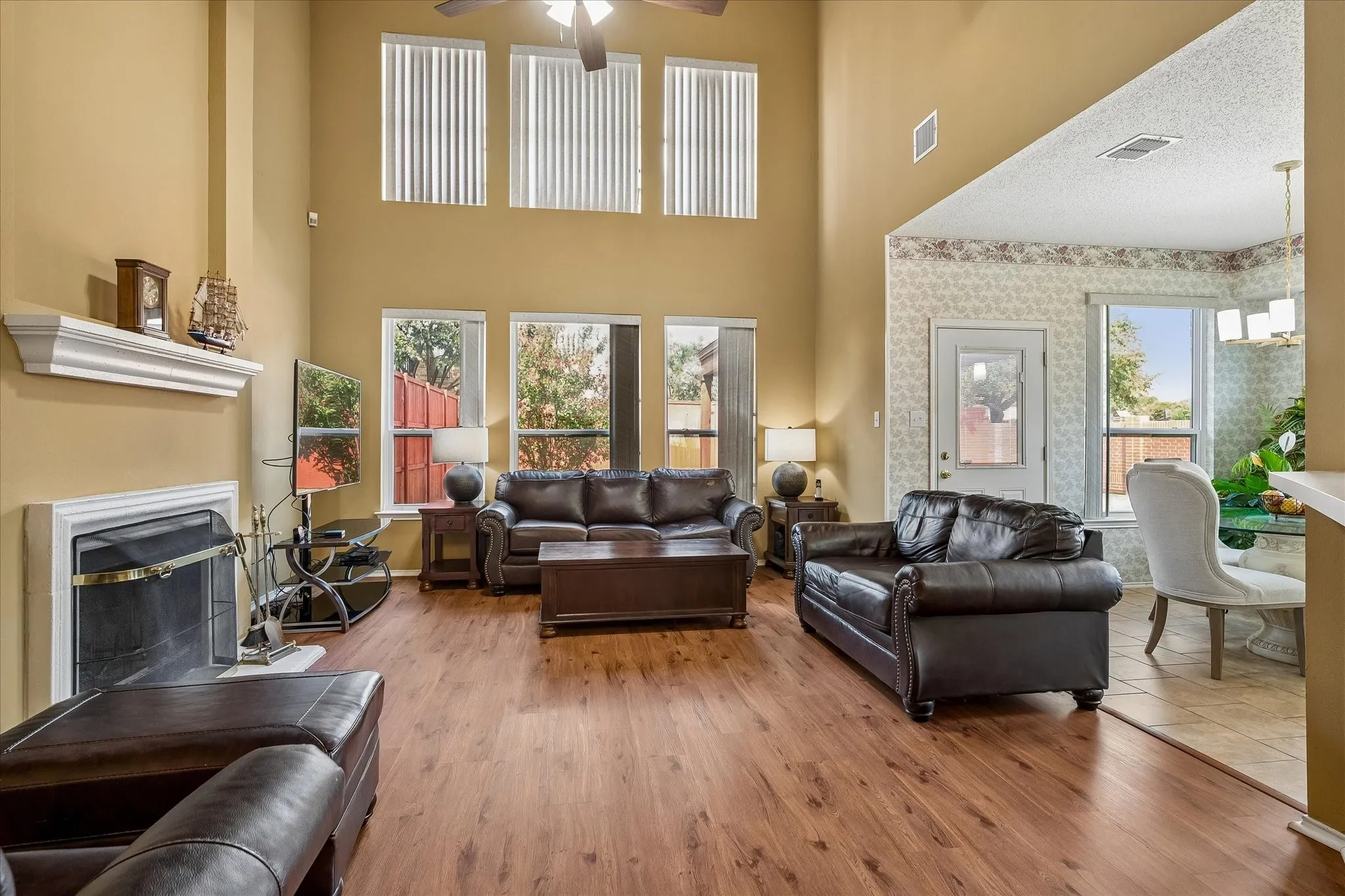 Two-story living area featuring a fireplace with a white mantel, wood-finish flooring, and multiple windows