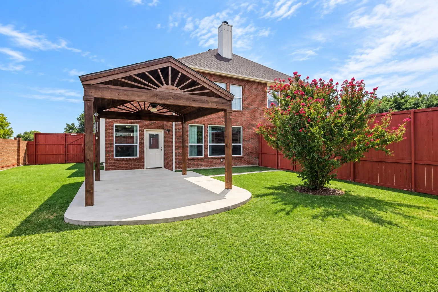 Expansive backyard featuring a manicured lawn, a covered concrete patio with a wood pergola, and a brick exterior