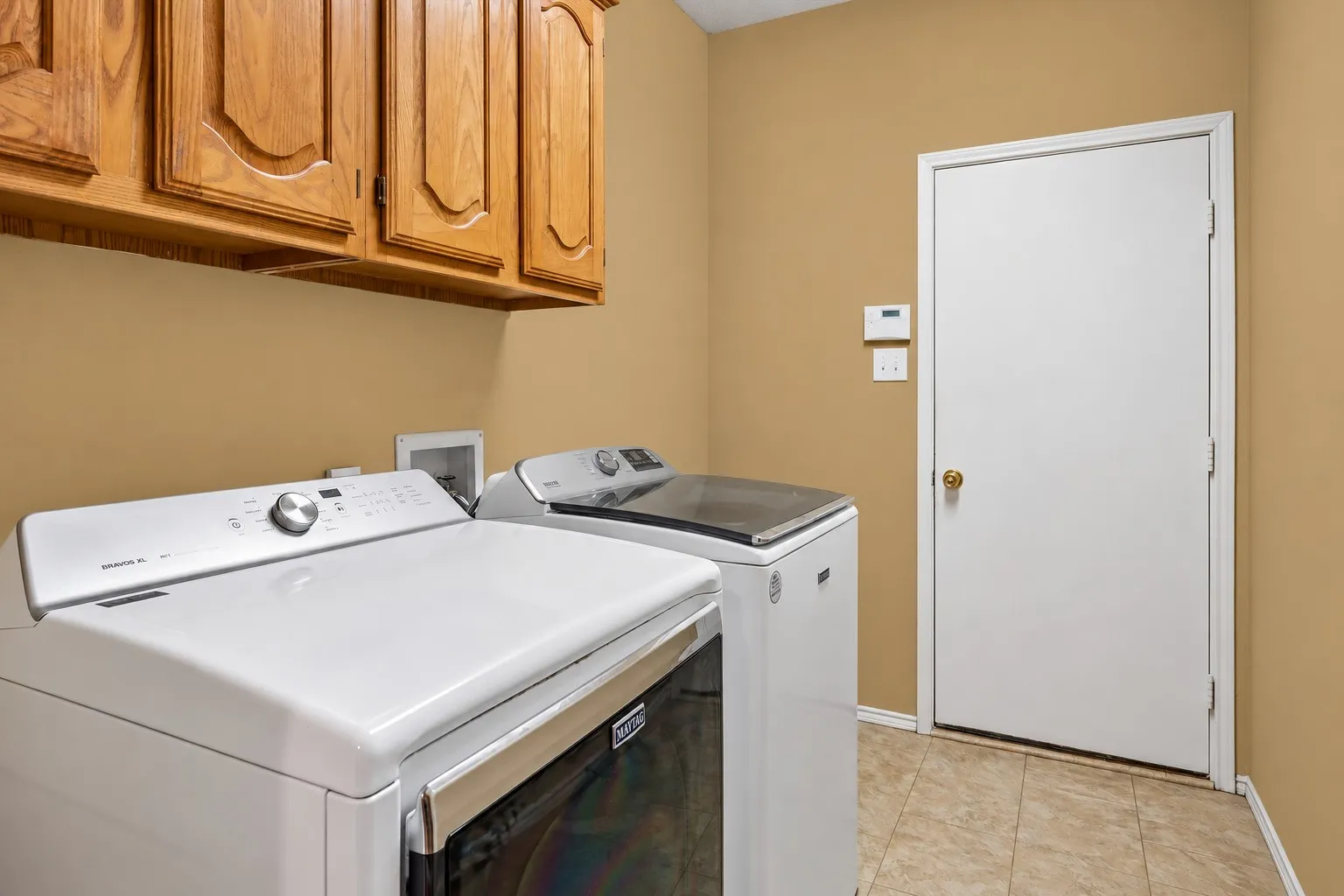 Laundry area with wood-finish upper cabinetry, a white door, and tiled flooring