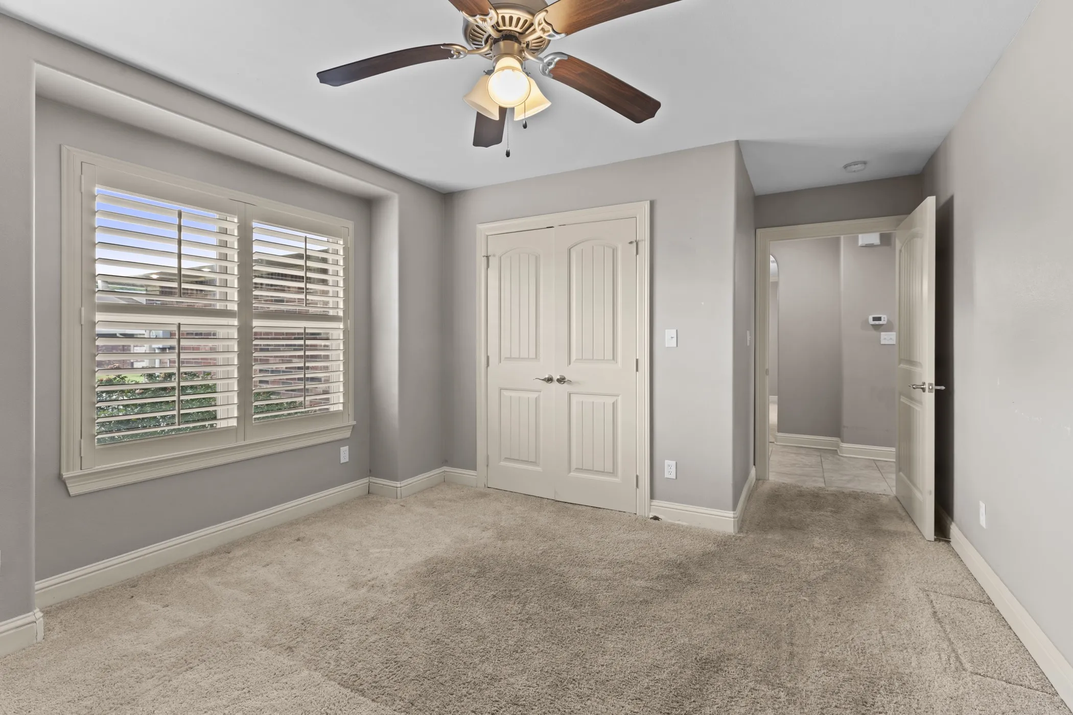 Carpeted room featuring a ceiling fan, window with white plantation shutters, and a double-door closet