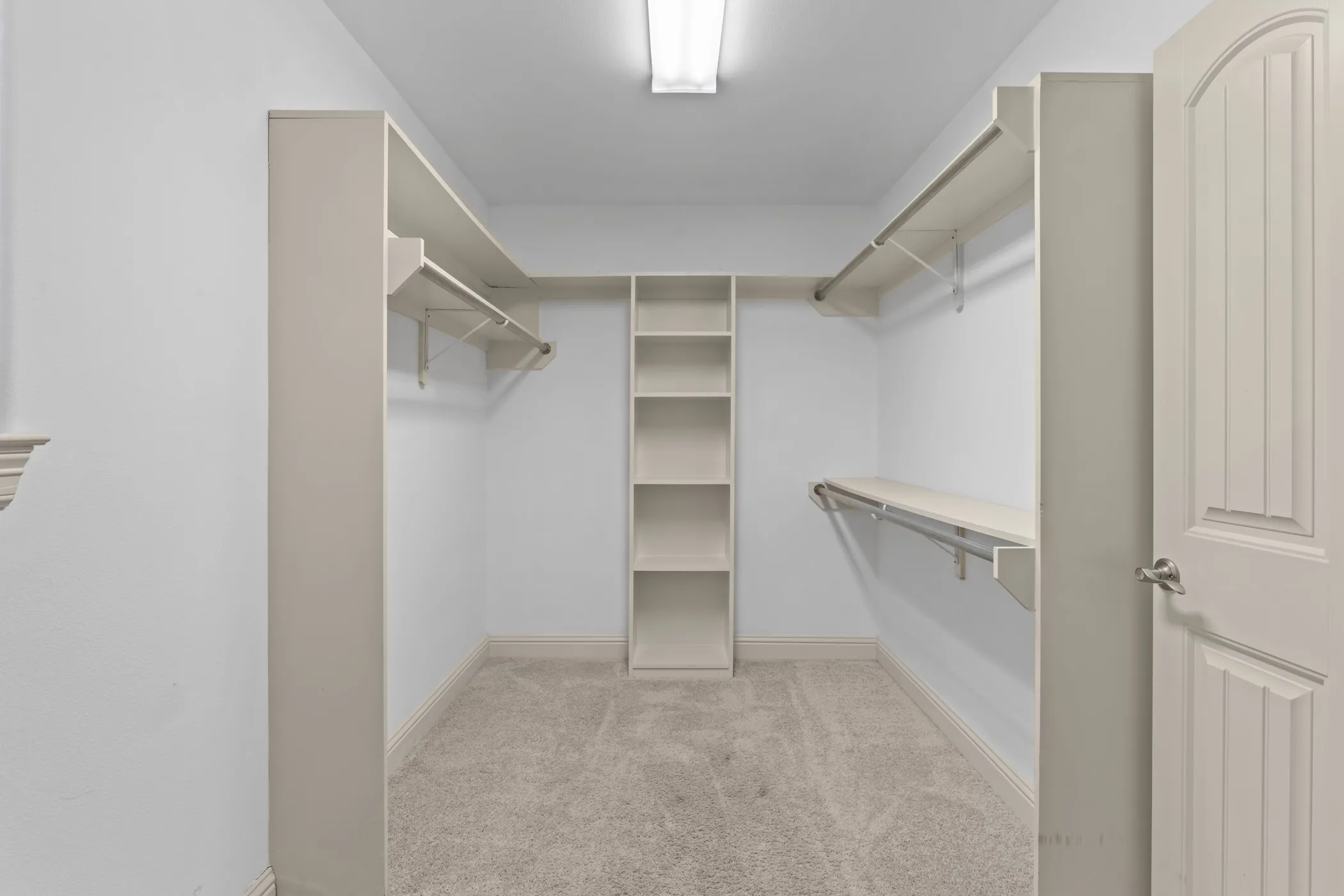 Built-in shelving, hanging rods, recessed lighting, and carpet flooring within a walk-in closet
