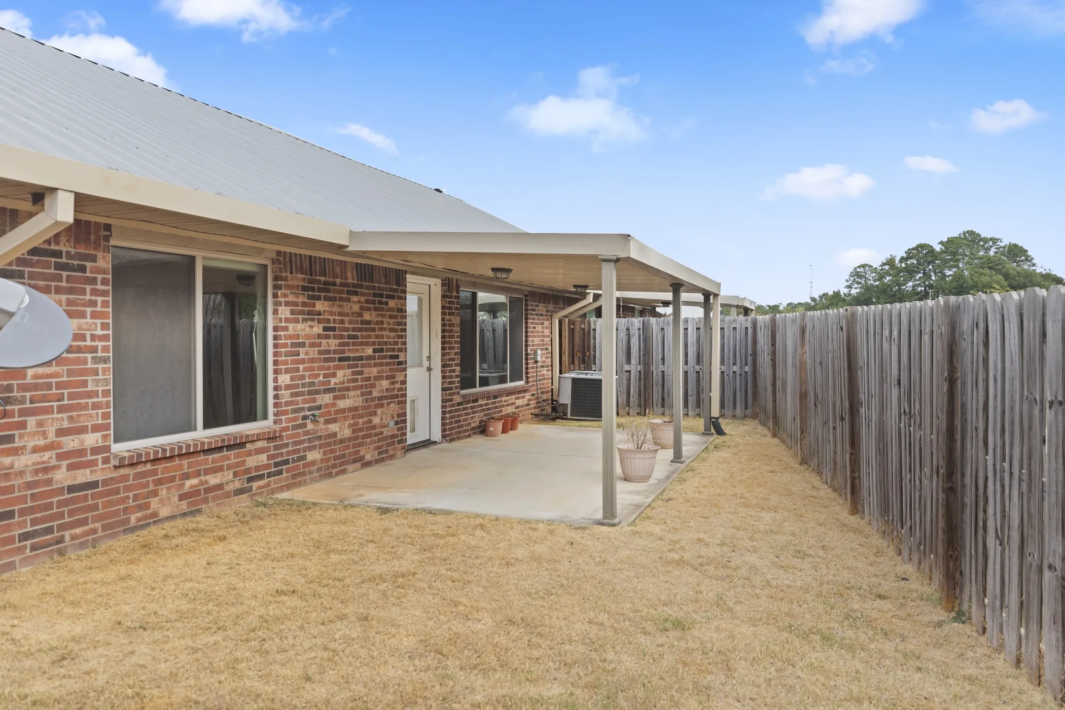 Brick exterior with a covered patio, concrete slab, and wood privacy fence