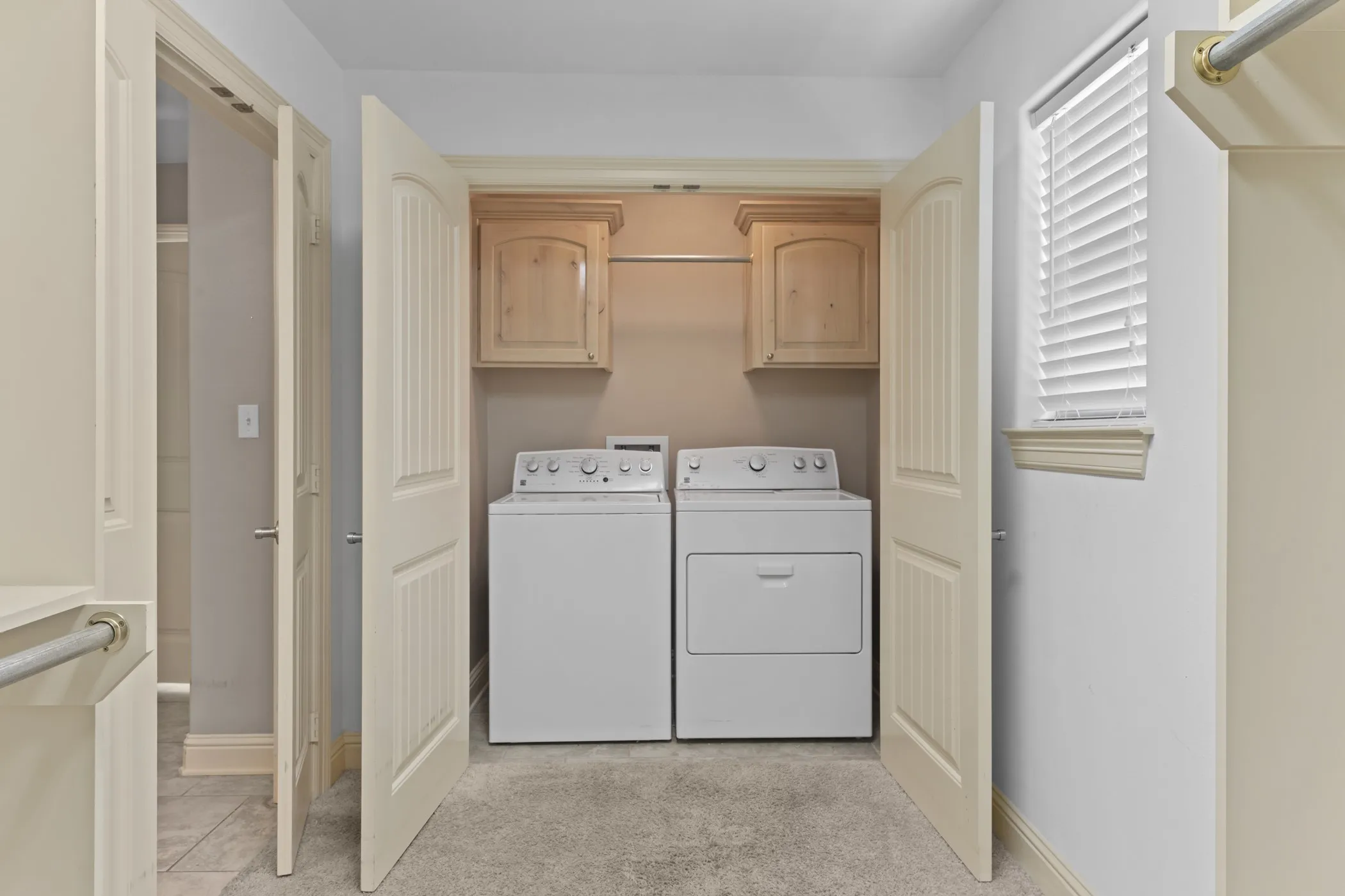 Laundry area featuring light wood-finish cabinetry, a chrome hanging rod, and carpet flooring