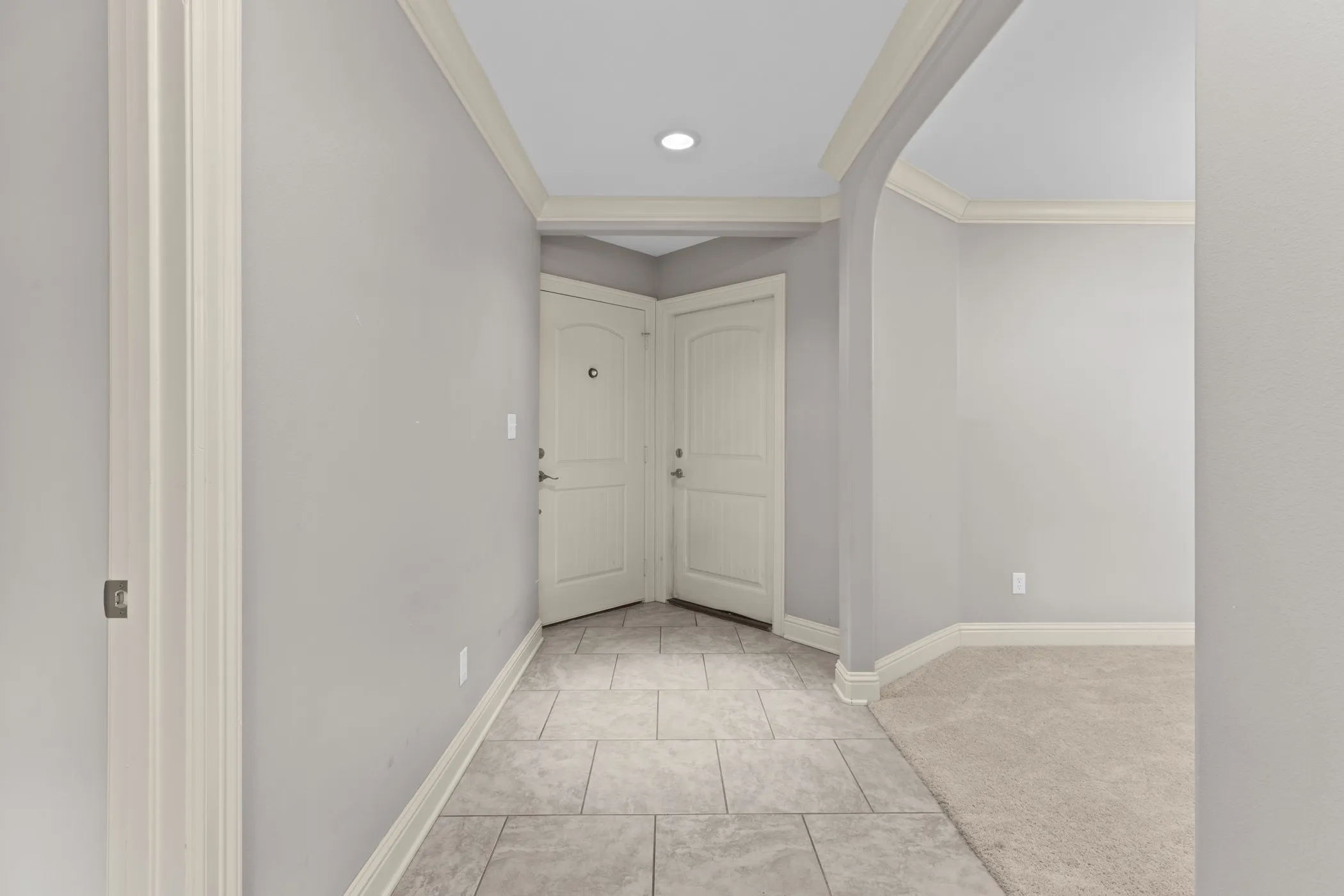 Recessed lighting illuminates the tiled entry, featuring two paneled doors and an arched doorway
