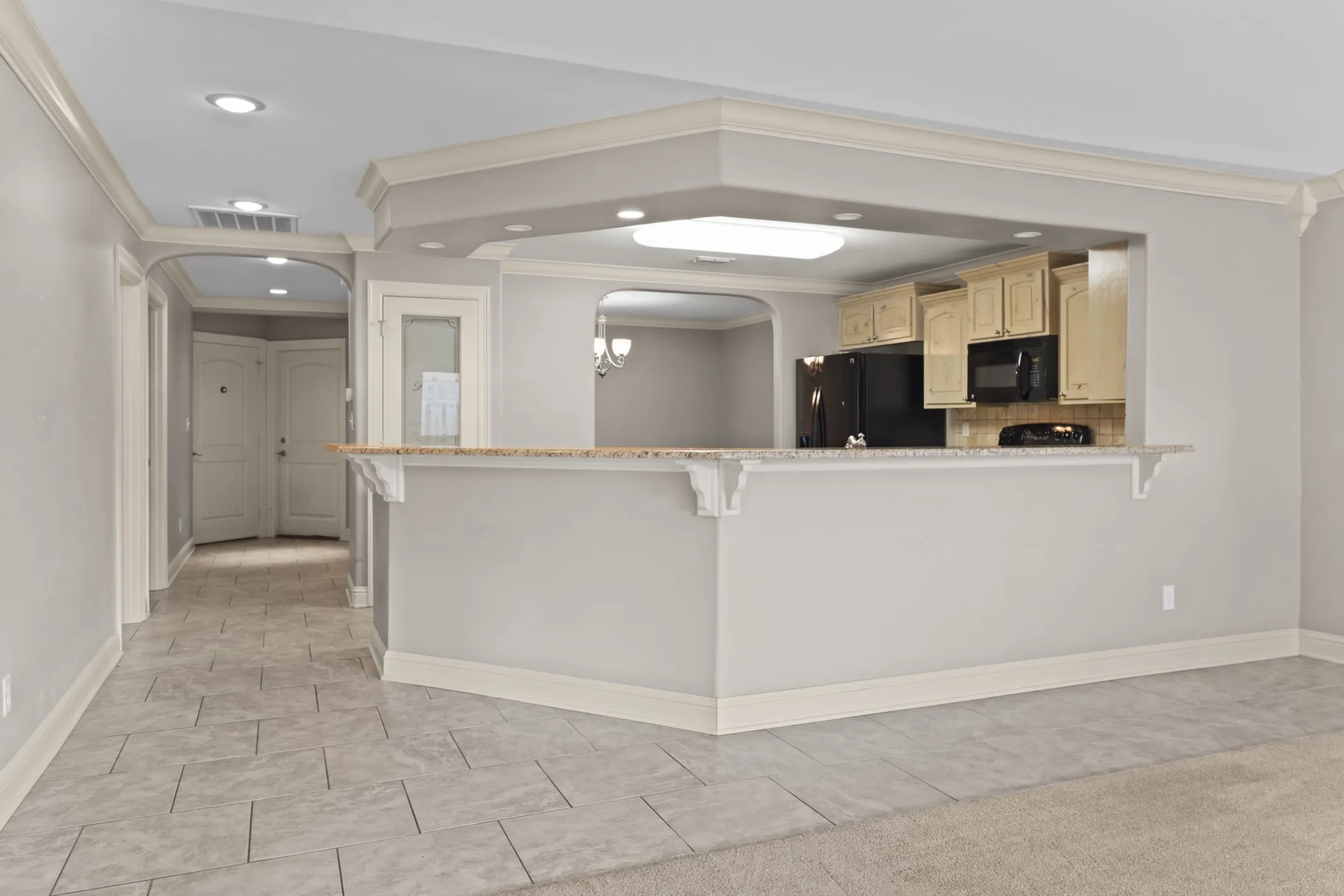 Kitchen pass-through with granite-look countertop, light wood-finish cabinetry, and black appliances
