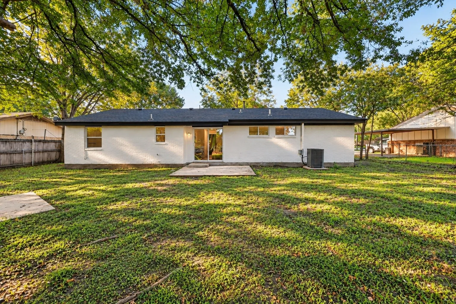 Expansive rear yard featuring a concrete patio, sliding glass door access, white brick exterior, and a dark shingle roof